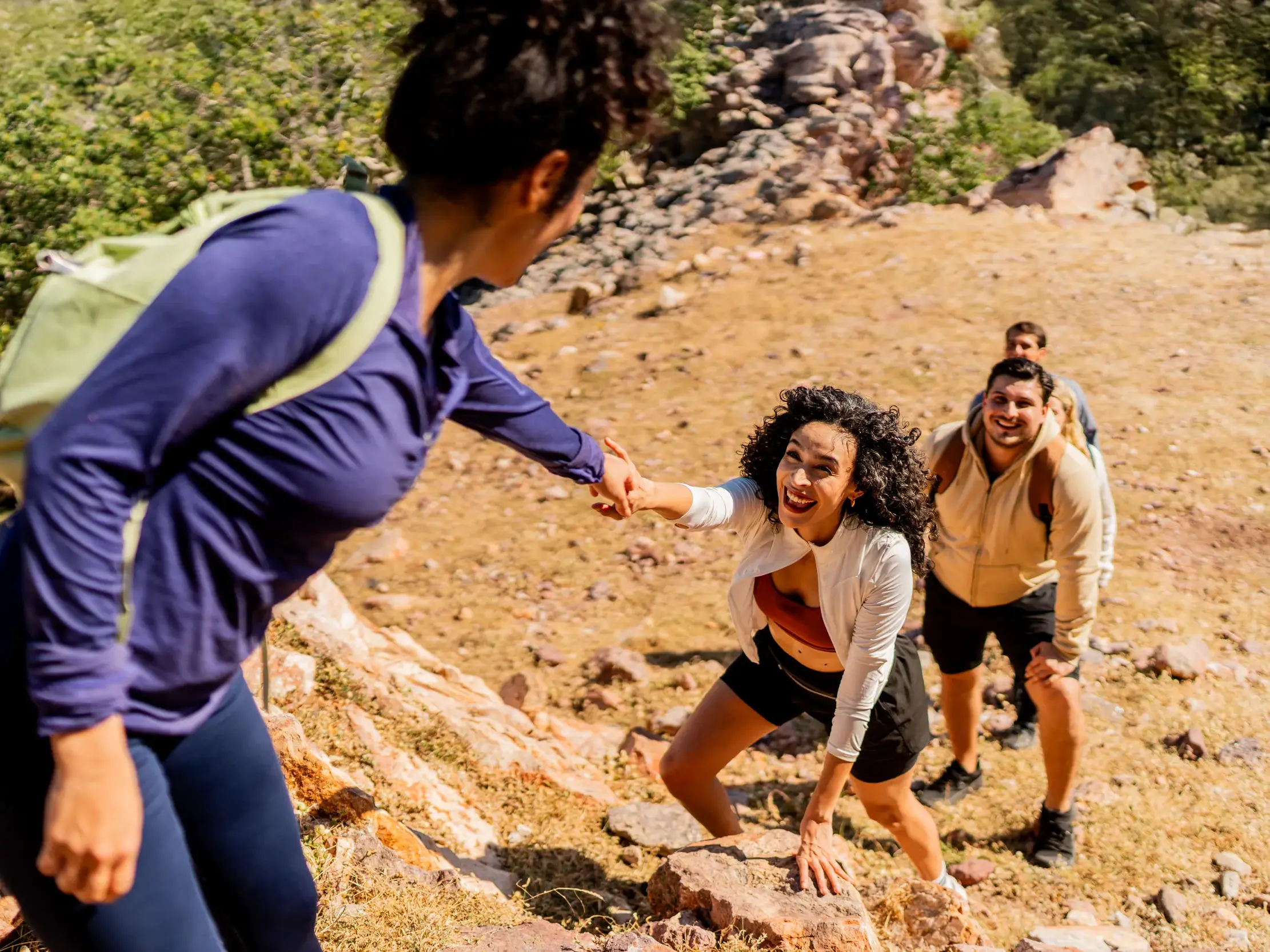 Eine lachende Frau bekommt auf einer Gruppenreise für junge Traveller Hilfe beim Klettern über Felsen im Nurataugebirge.