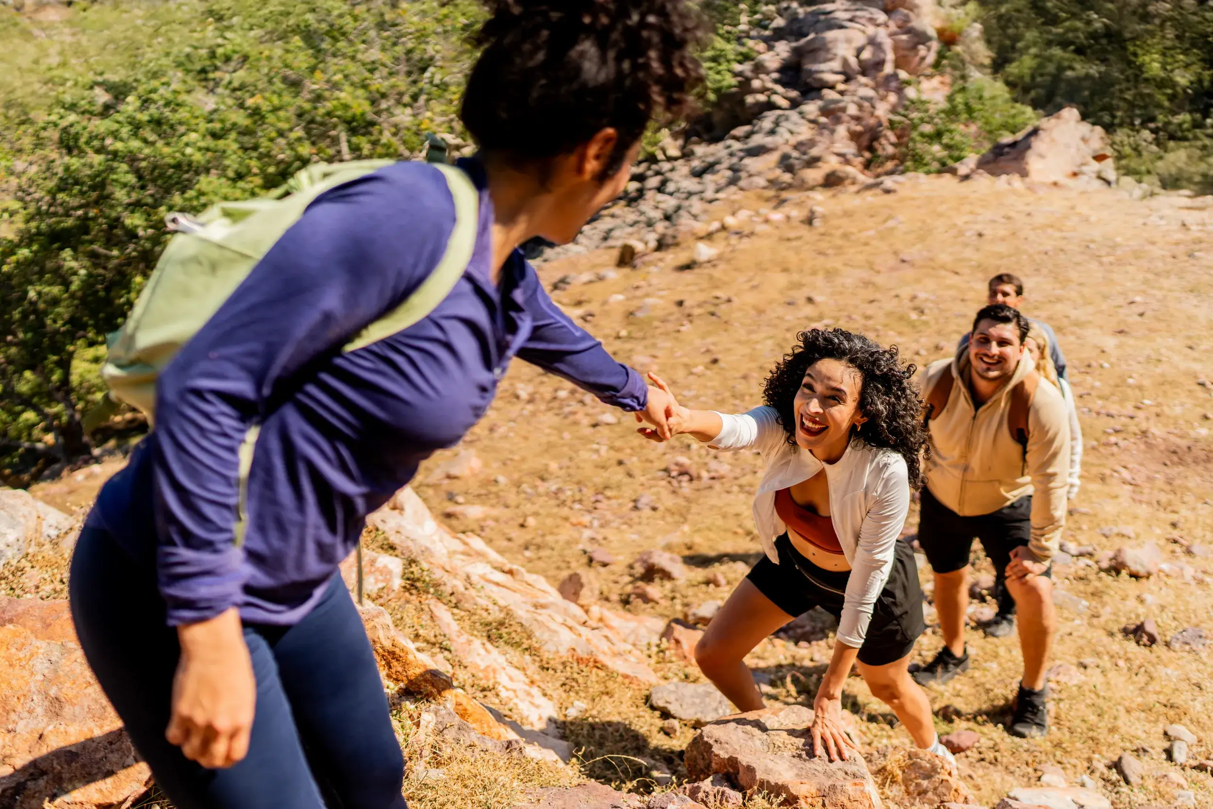 Eine lachende Frau bekommt auf einer Gruppenreise für junge Traveller Hilfe beim Klettern über Felsen im Nurataugebirge.