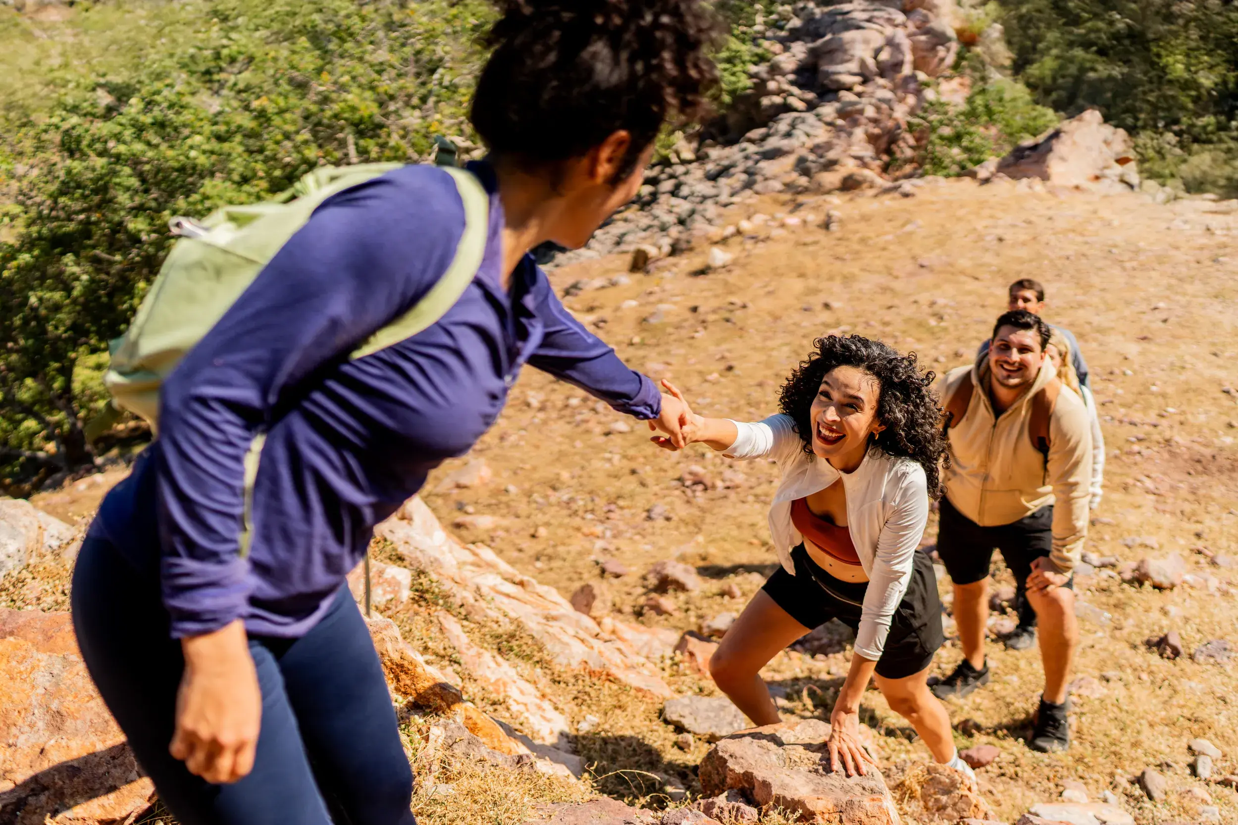 Eine lachende Frau bekommt auf einer Gruppenreise für junge Traveller Hilfe beim Klettern über Felsen im Nurataugebirge.