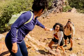 Eine lachende Frau bekommt auf einer Gruppenreise für junge Traveller Hilfe beim Klettern über Felsen im Nurataugebirge.