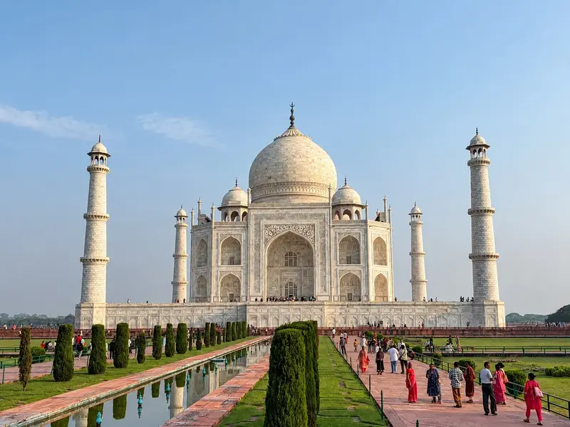 Das prachtvolle Taj Mahal in Agra an einem sonnigen Tag. Besucher spazieren entlang des Wasserkanals durch die Gartenanlage.