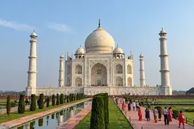 Das prachtvolle Taj Mahal in Agra an einem sonnigen Tag. Besucher spazieren entlang des Wasserkanals durch die Gartenanlage.