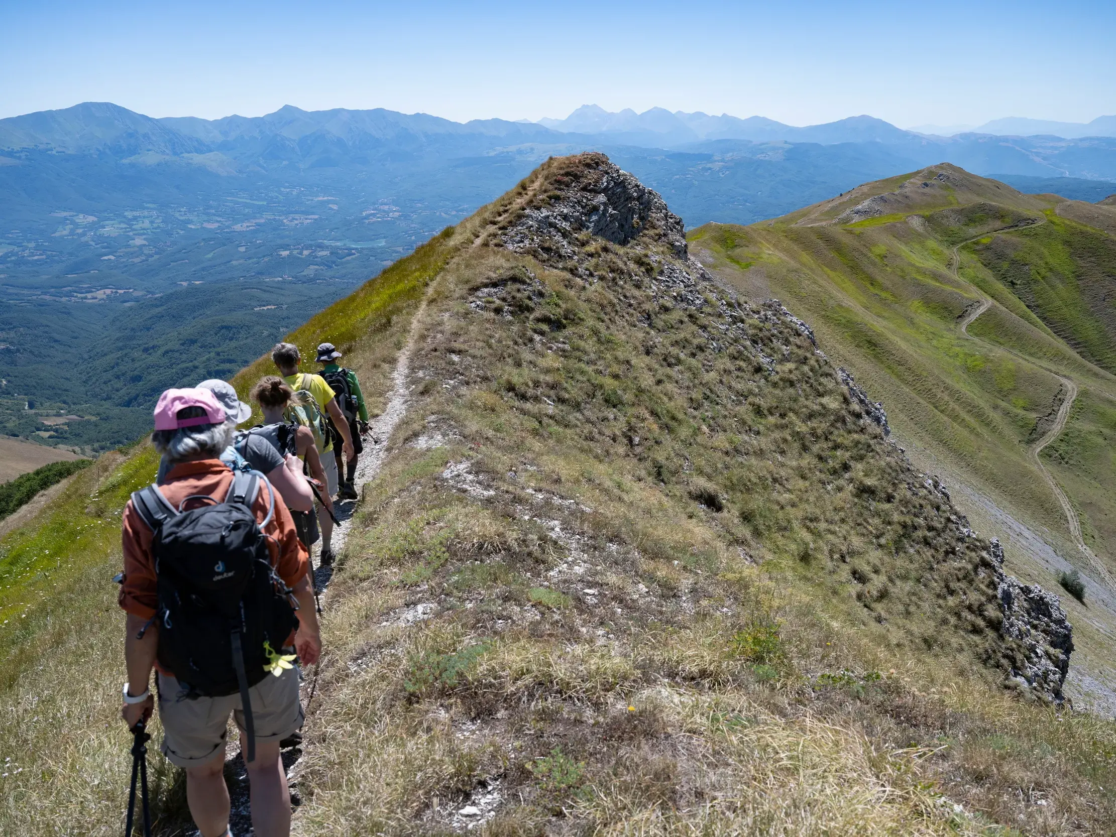 Eine Wandergruppe bei einer Gratwanderung auf einem schmalen Pfad in den Sibillinischen Bergen mit Panoramablick auf den Apennin.