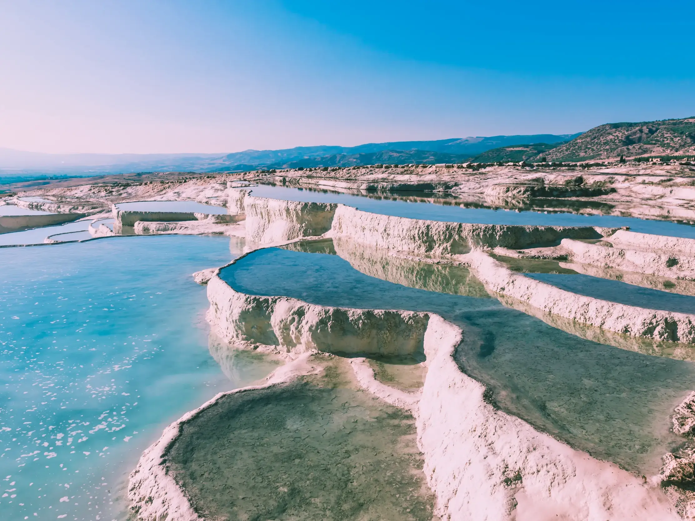 Die porzellanweißen Sinterterrassen von Pamukkale, gefüllt mit türkisblauem Thermalwasser, unter der Sonne der Türkei.