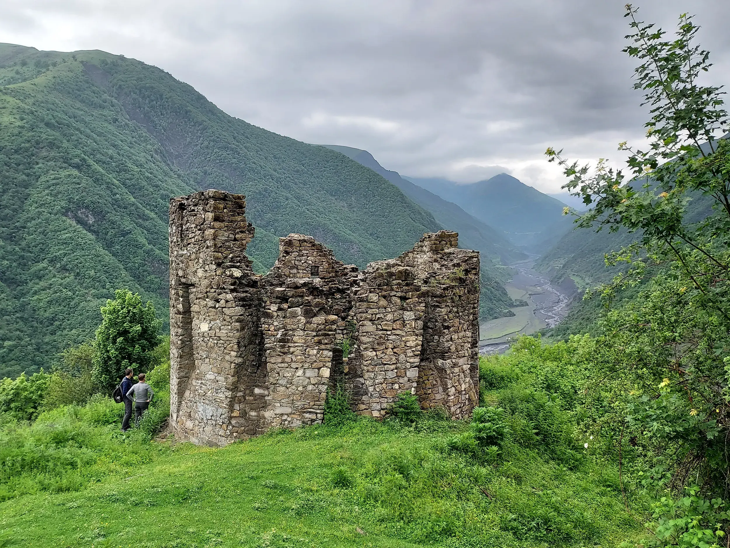 Steinruine des Forts Shamil-Gala in der Region Qax mit zwei Wanderern und weitem Blick ins Tal des Großen Kaukasus.