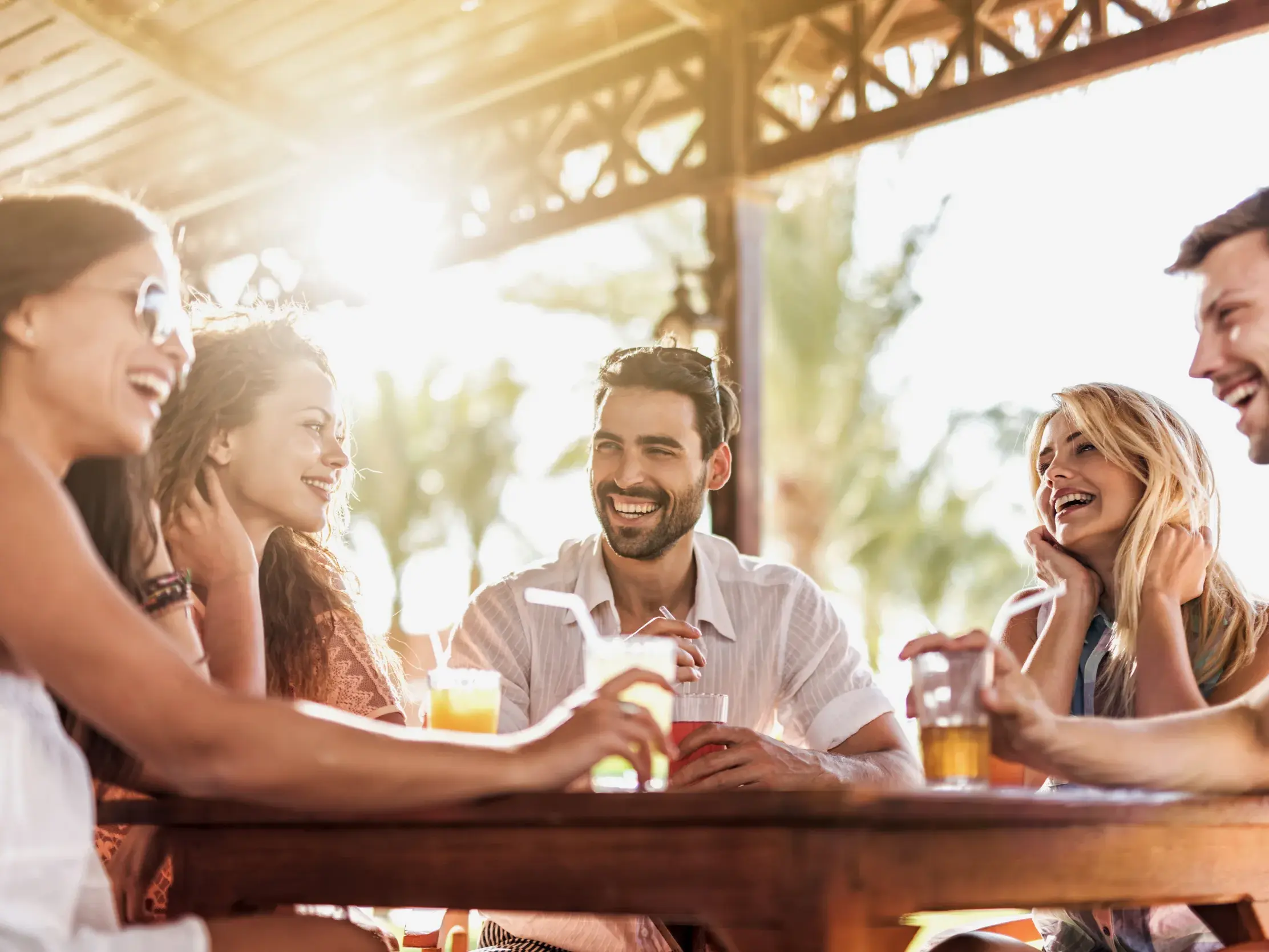 Eine gut gelaunte Kleingruppe junger Leute genießt lachend Cocktails in einer Bar während ihrer Rundreise in Thailand.