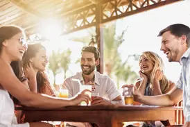 Eine gut gelaunte Kleingruppe junger Leute genießt lachend Cocktails in einer Bar während ihrer Rundreise in Thailand.