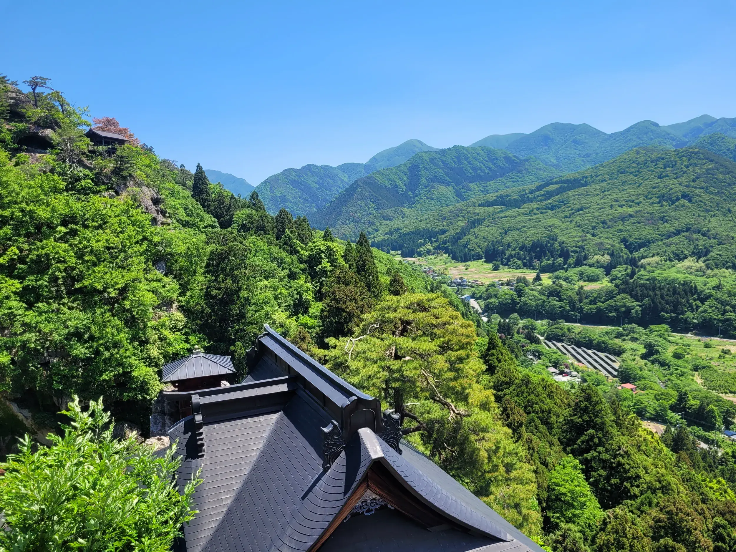 Weitreichender Blick vom Yamadera Tempelkomplex über ein dicht bewaldetes Tal und grüne Berge in der Präfektur Yamagata, Japan.