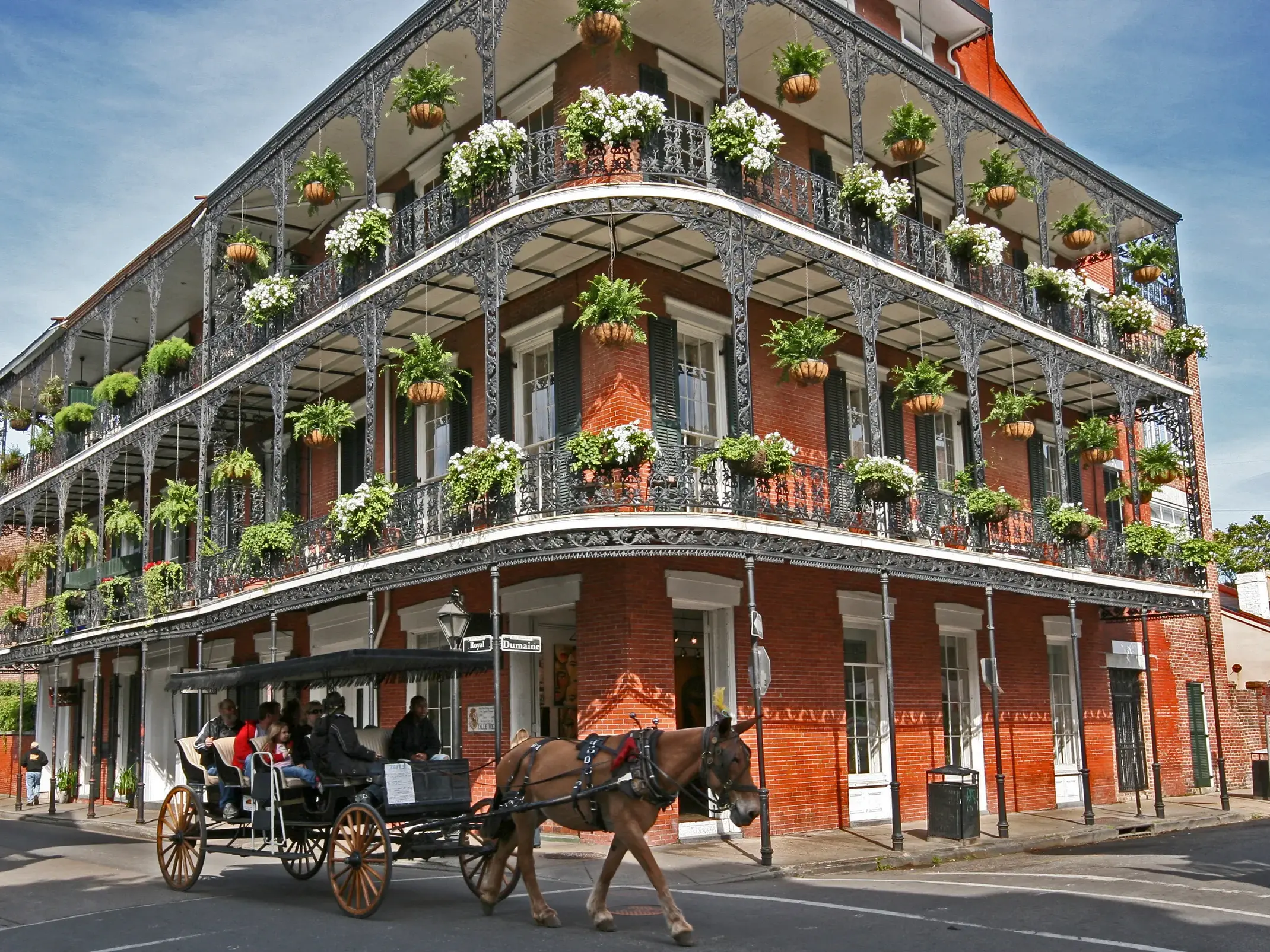 Eine Pferdekutsche fährt an einem historischen Eckhaus mit blumengeschmückten, schmiedeeisernen Balkonen im French Quarter von New Orleans.