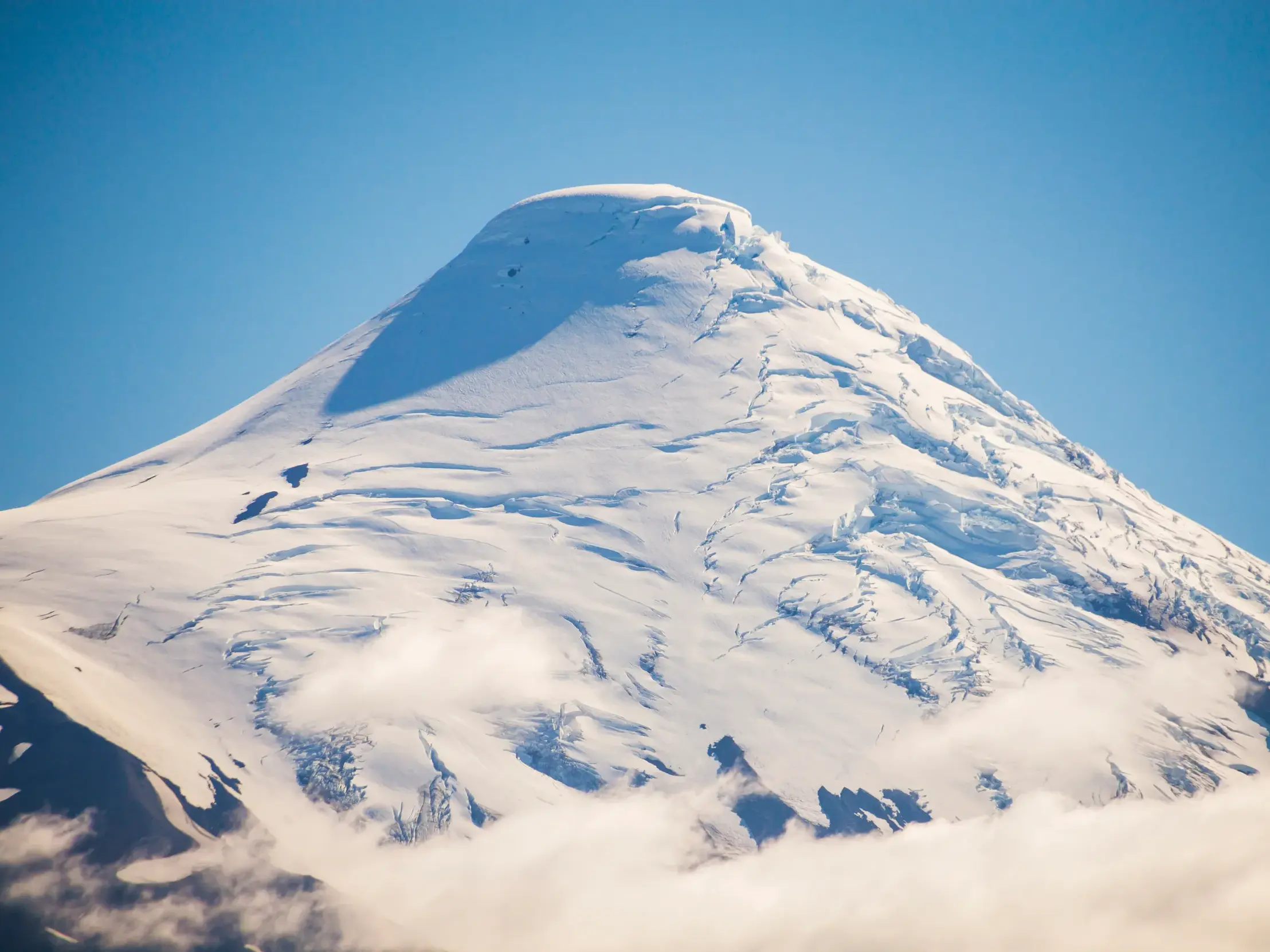 Der schneebedeckte Gipfel des Vulkans Osorno in Nordpatagonien ragt bei strahlend blauem Himmel über den Wolken empor.