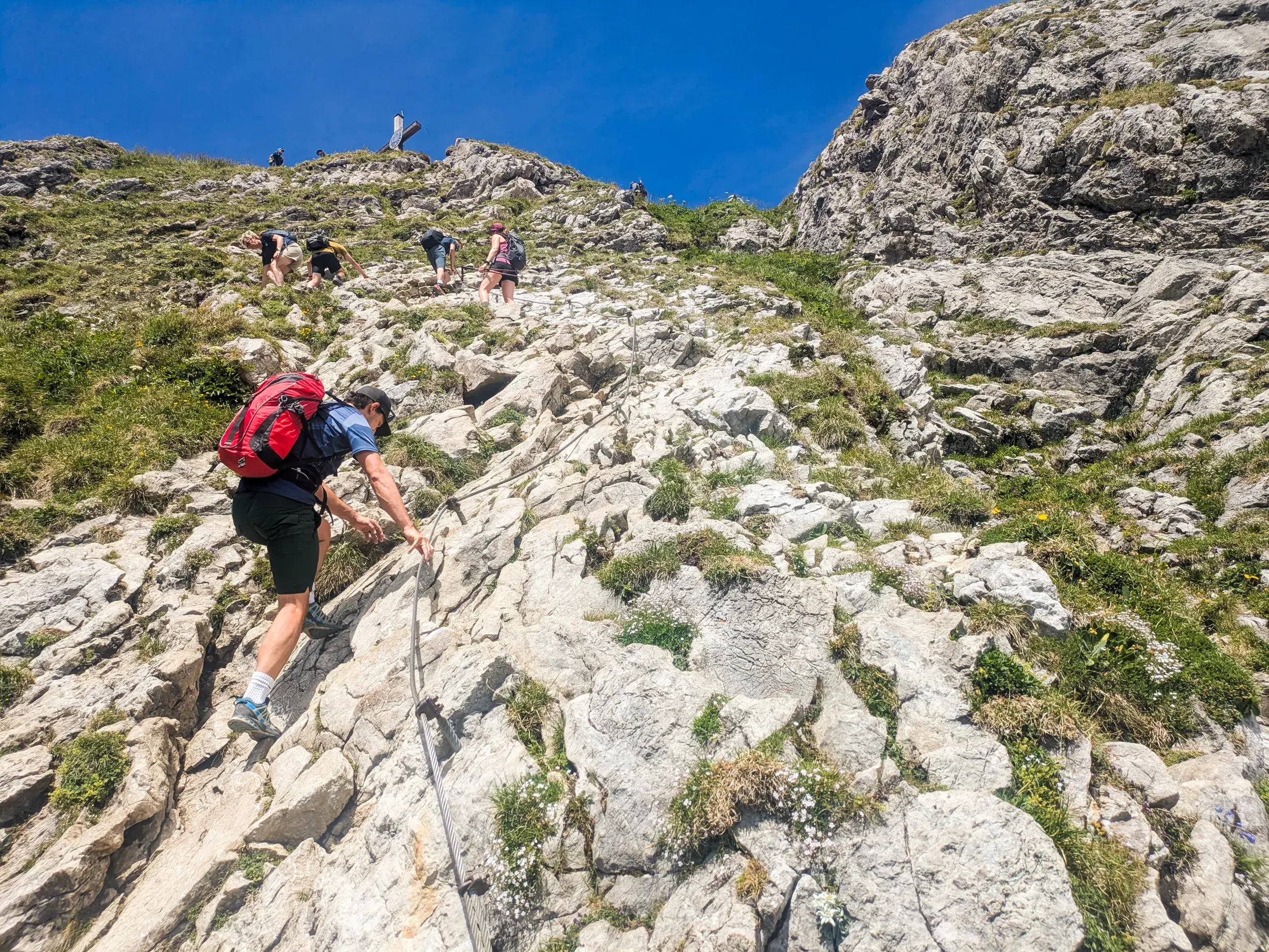 Eine Wandergruppe beim anspruchsvollen Aufstieg zum Aggenstein, gesichert durch ein Drahtseil am felsigen Steig.