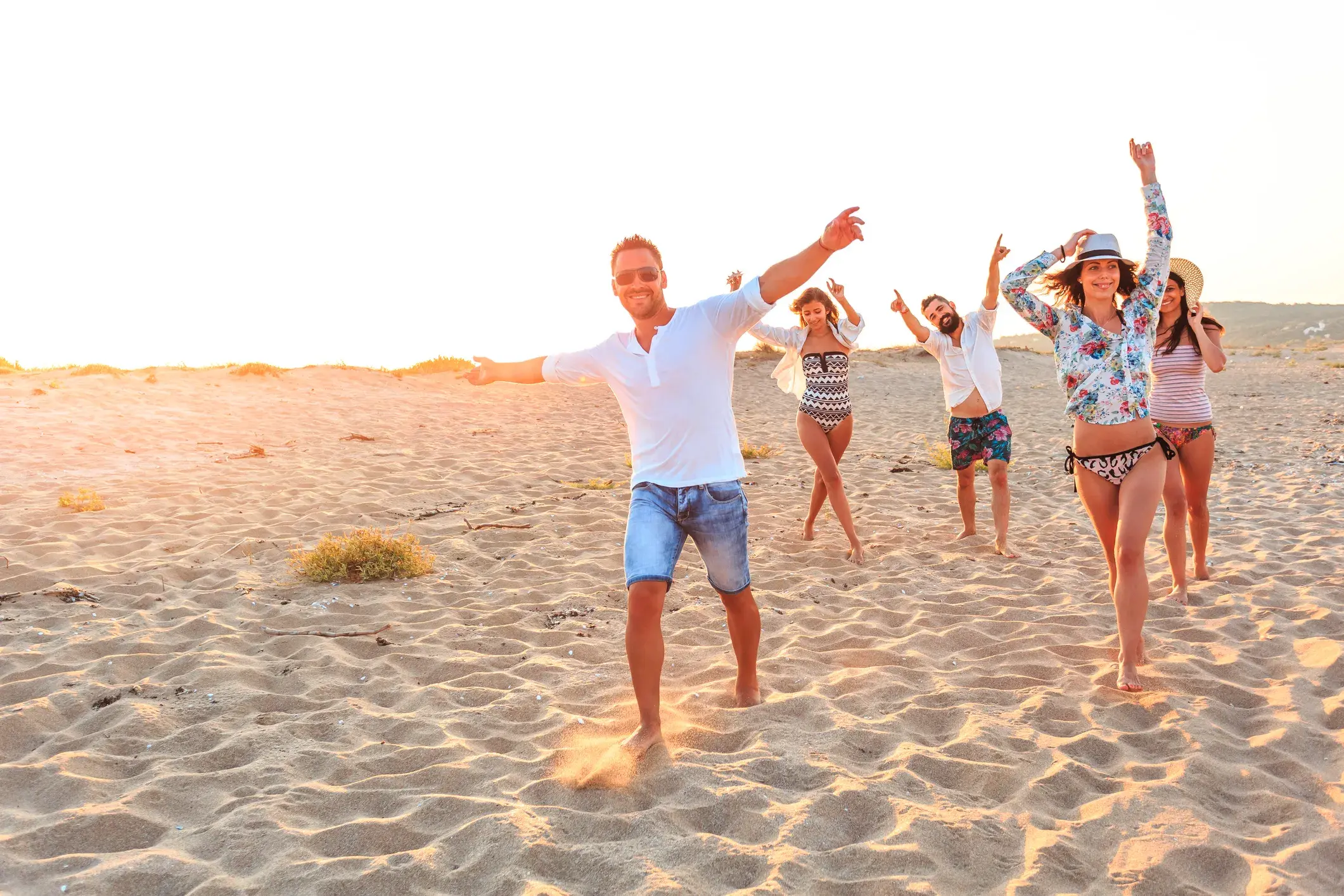 Eine Gruppe junger Leute feiert ausgelassen am Strand bei Sonnenuntergang während einer Gruppenreise für junge Leute in Indonesien.