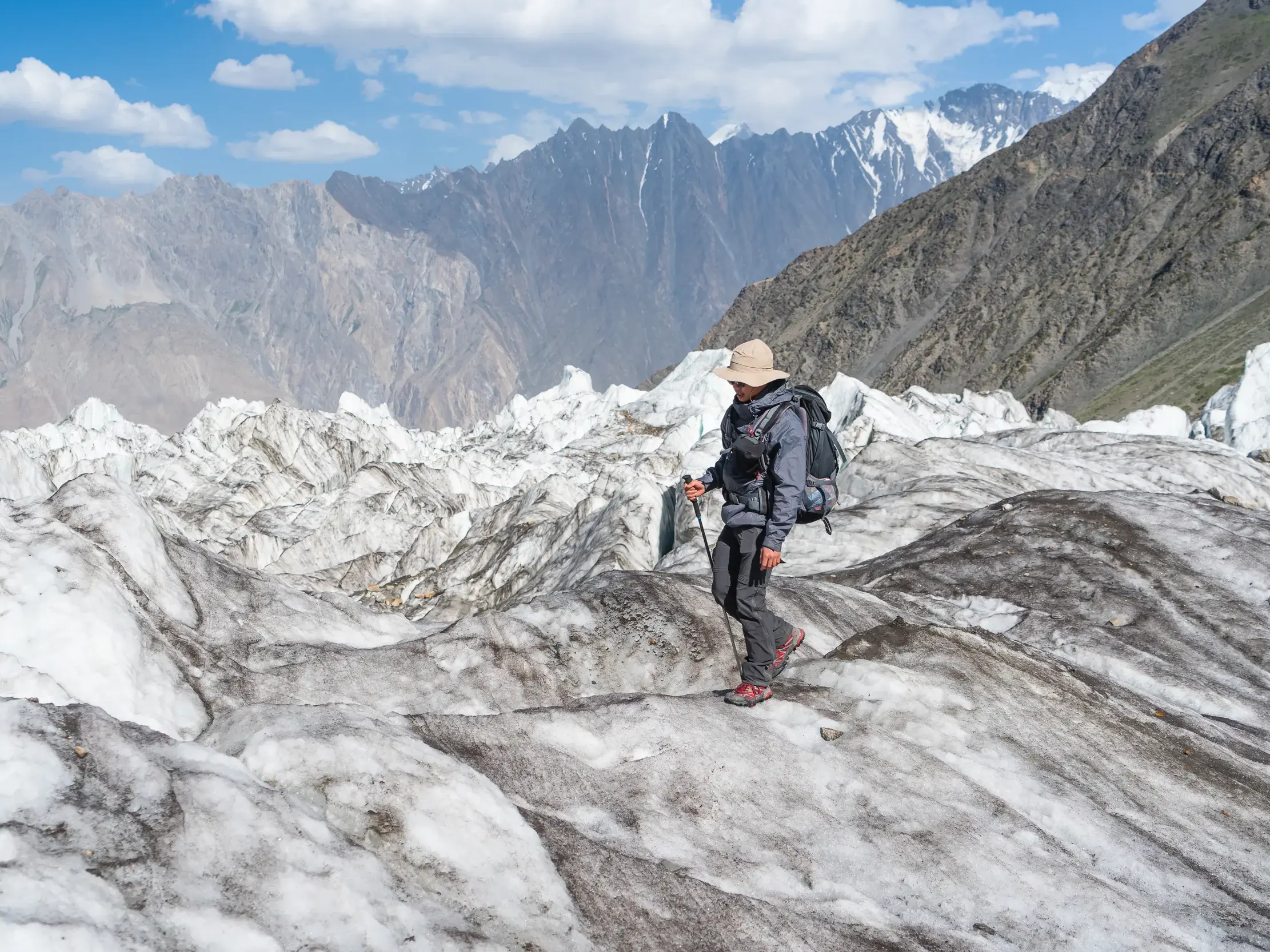 Ein Trekker mit Rucksack und Hut wandert über den Gulkin-Gletscher vor der Bergkulisse des Karakorum in Pakistan.