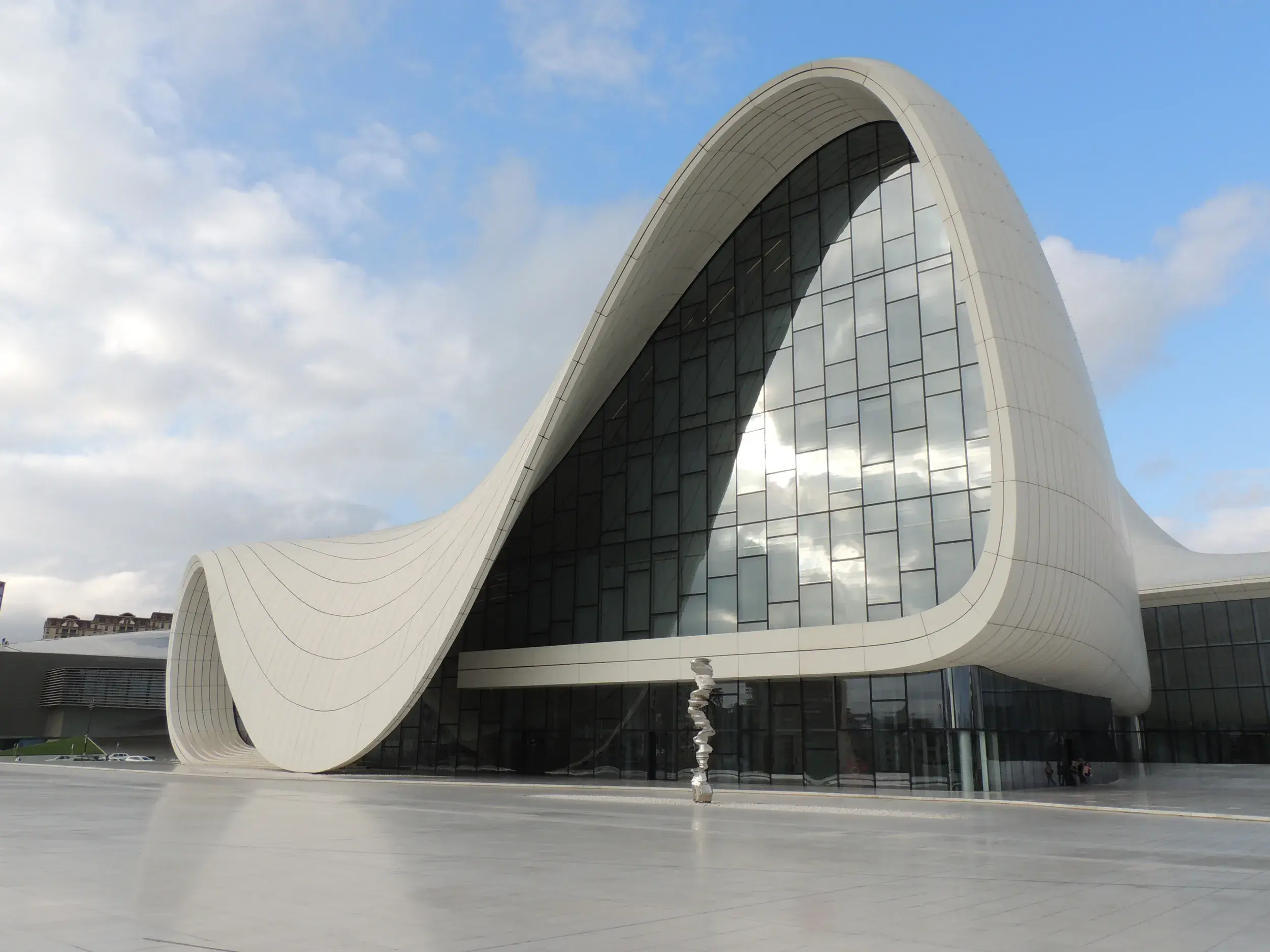 Die weiße, fließende Architektur des Heydar-Aliyev-Zentrums in Baku spiegelt sich auf dem nassen Vorplatz wider.