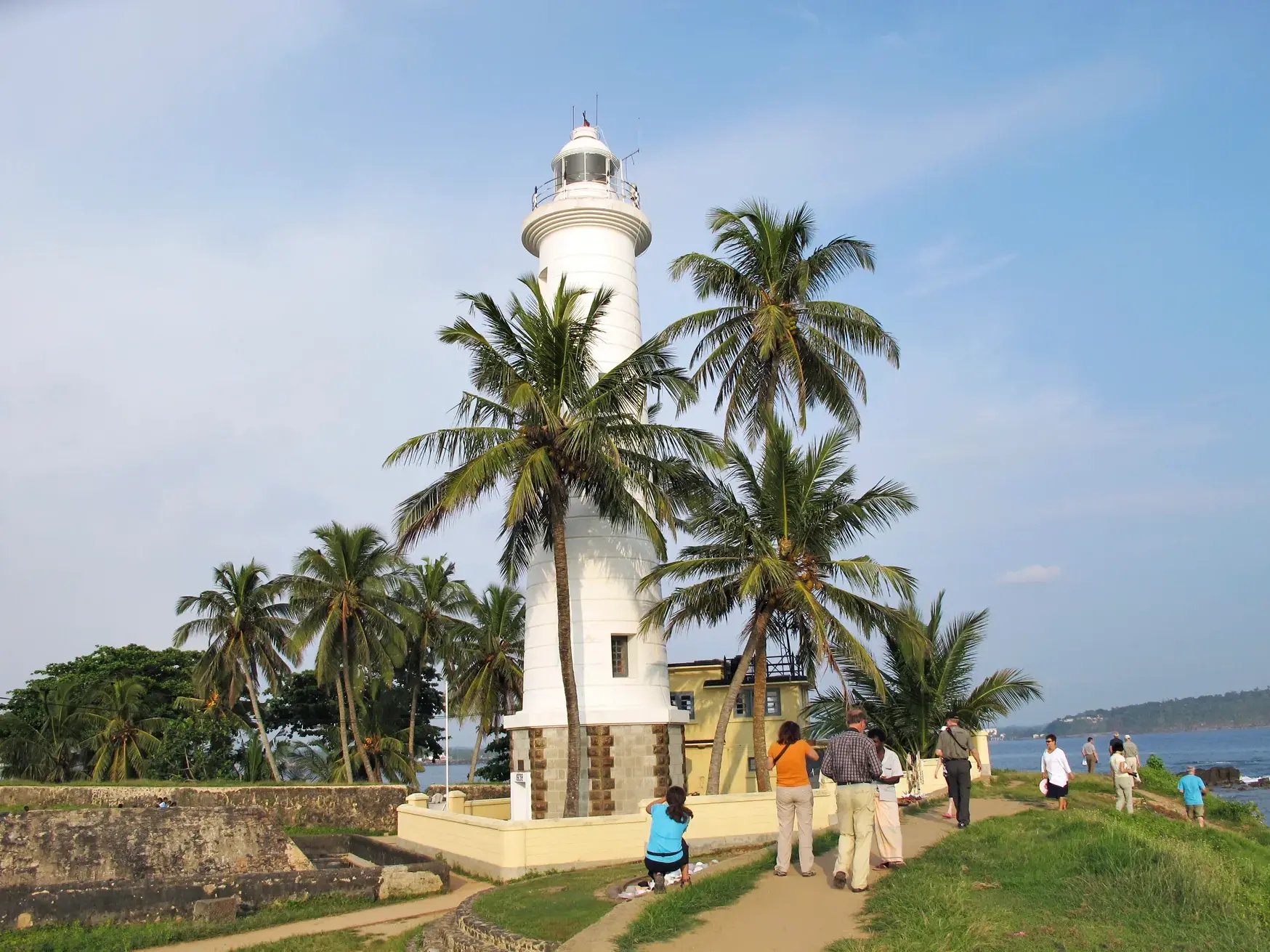 Eine Reisegruppe erkundet zu Fuß den historischen Leuchtturm im Galle Fort, umgeben von Palmen an der Küste Sri Lankas.