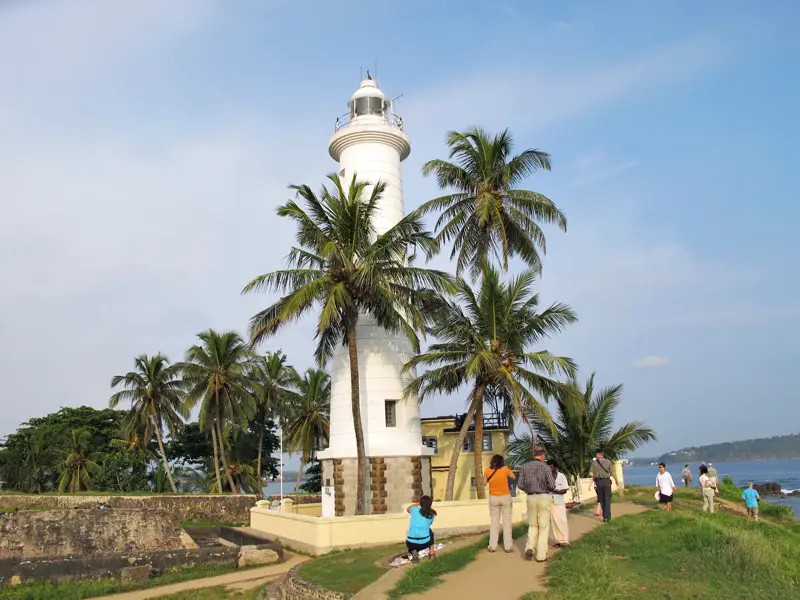Eine Reisegruppe erkundet zu Fuß den historischen Leuchtturm im Galle Fort, umgeben von Palmen an der Küste Sri Lankas.