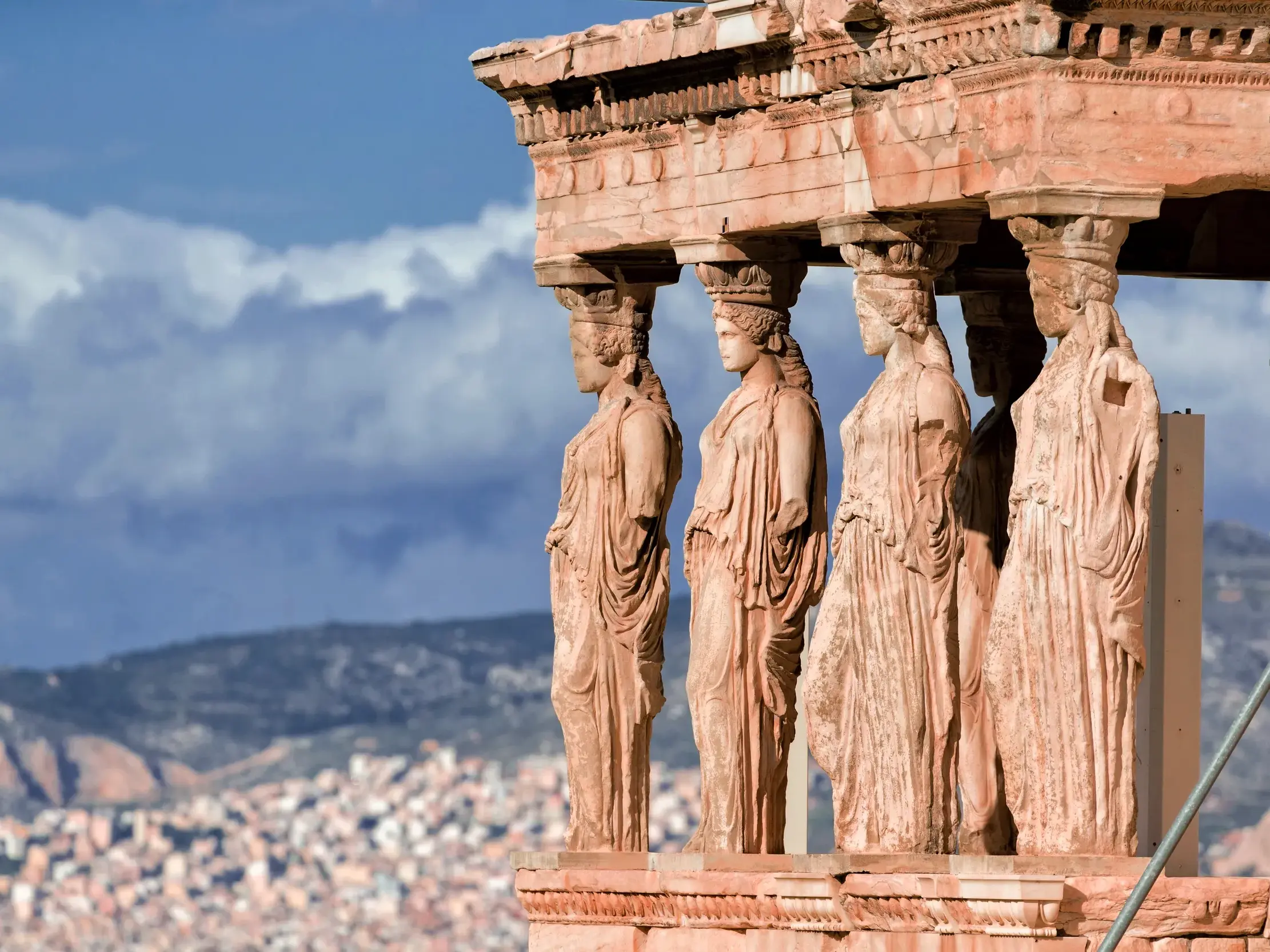 Die berühmten Karyatiden des Erechtheion auf der Akropolis in Athen mit Panoramablick über die Stadt bei blauem Himmel.