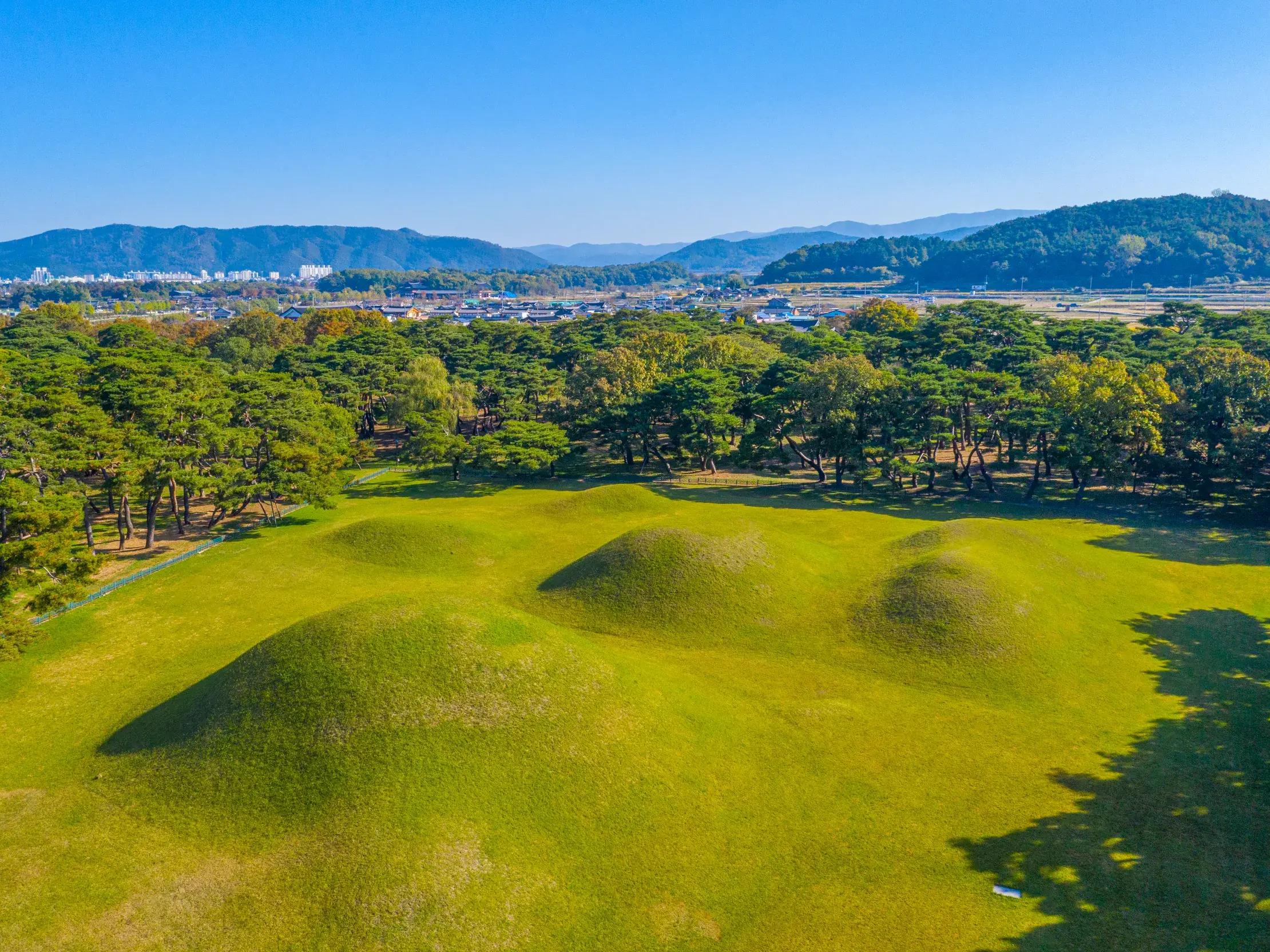 Luftaufnahme der mystischen, grasbewachsenen Königsgräber im Tumuli-Park von Gyeongju vor einer Bergkulisse in Südkorea.