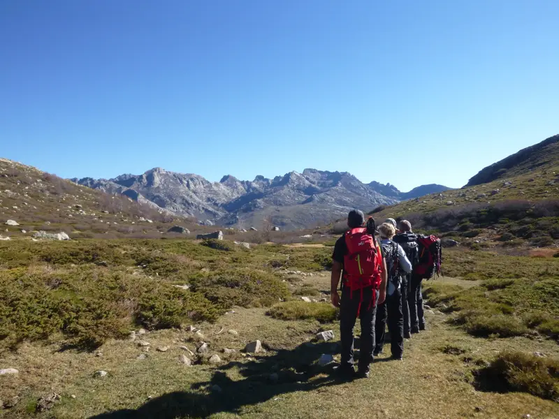 Eine kleine Wandergruppe auf dem Fernwanderweg GR 20 beim Trekking durch die weite, sonnige Berglandschaft Korsikas.