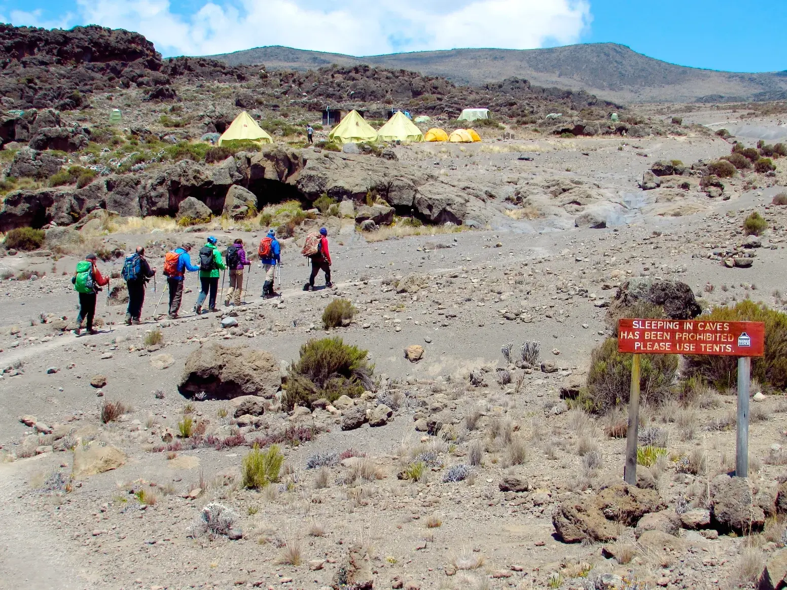 Eine Hauser-Reisegruppe wandert auf einem Pfad durch die karge Hochgebirgslandschaft des Kilimanjaro auf ihr Zeltlager zu.
