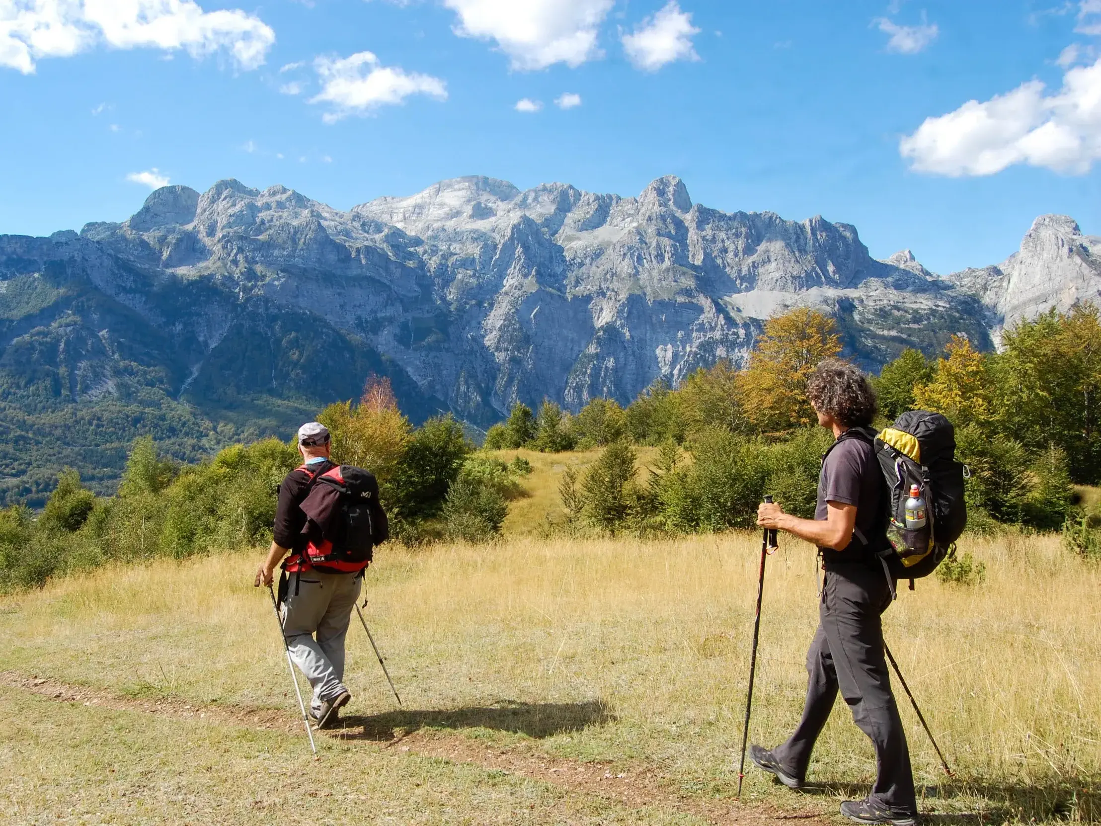 Zwei Trekking-Reisende wandern auf dem Peaks of the Balkans Trail mit Blick auf die gezackten Gipfel der Bjeshket e Namuna.