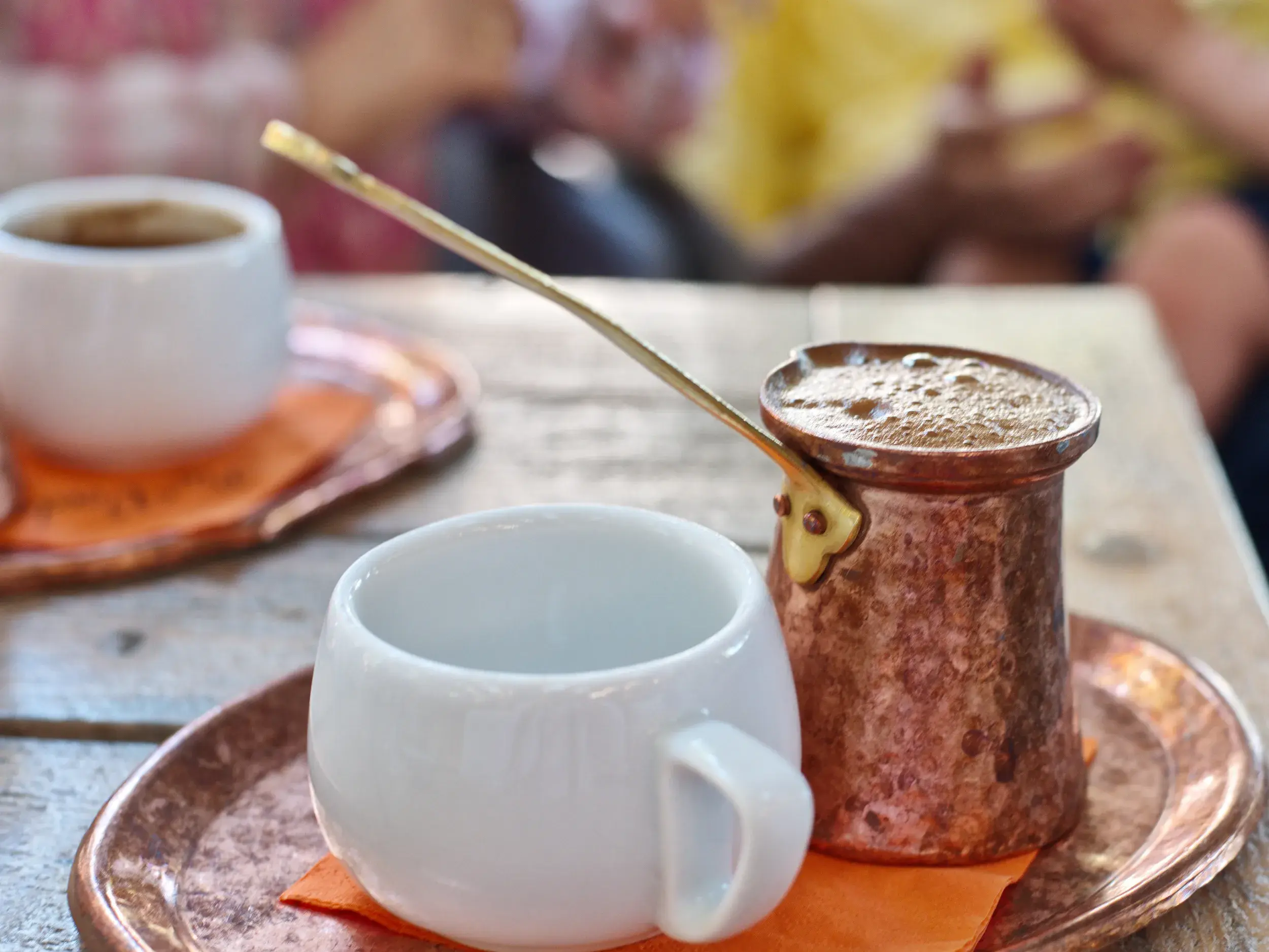 Ein Kupferkännchen mit frisch aufgebrühtem griechischem Kaffee und Tassen auf dem Tisch einer landestypischen Taverne in Griechenland.
