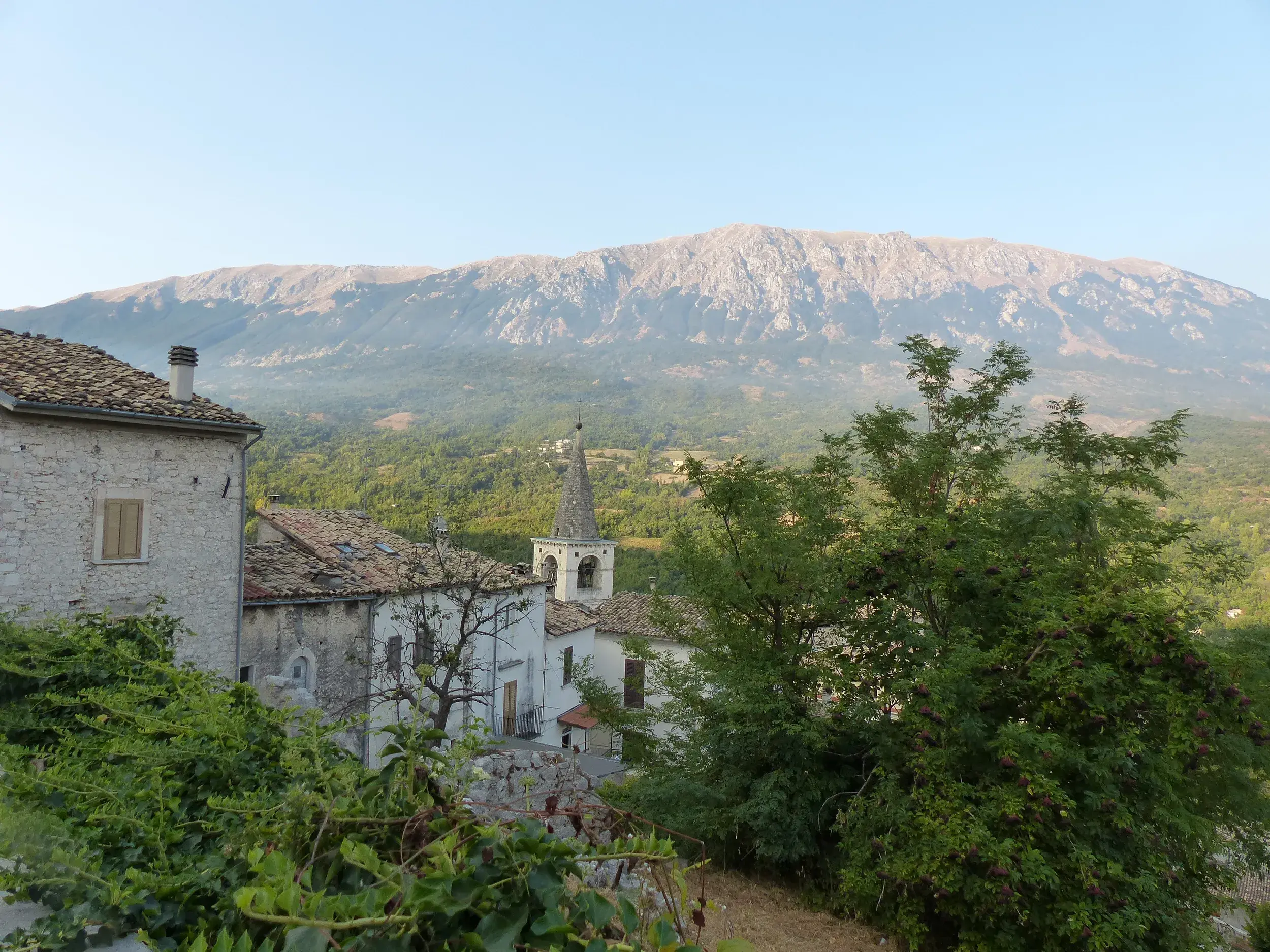 Rustikale Steinhäuser eines Bergdorfs in den Abruzzen mit Blick auf die bewaldeten Hänge und Gipfel des Gran Sasso Massivs.
