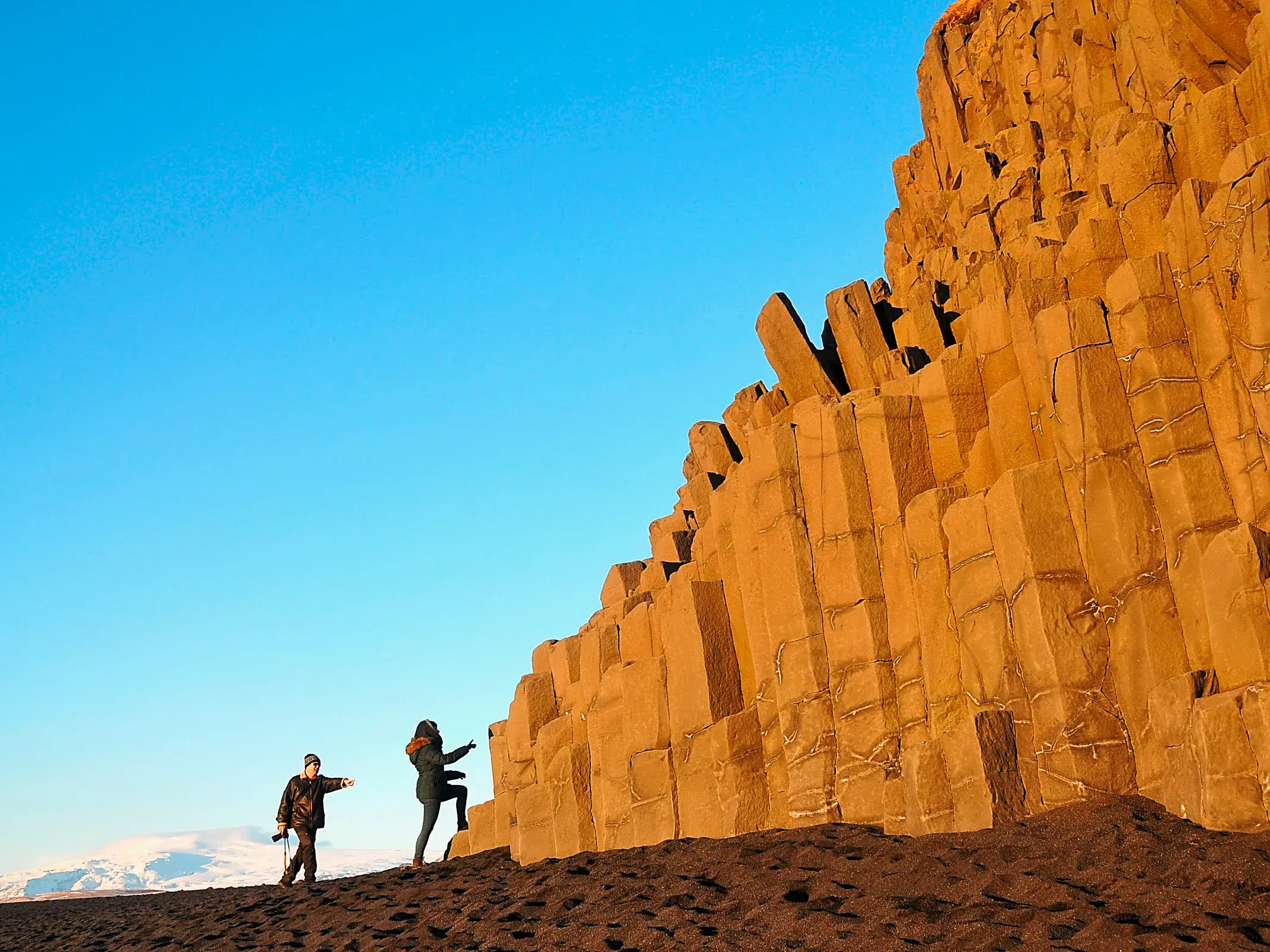 Zwei Teilnehmer einer Kleingruppenreise erkunden die goldenen Basaltsäulen von Reynisfjara am schwarzen Strand in Südisland.