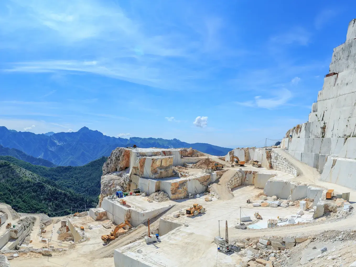 Die beeindruckenden, terrassierten Marmorsteinbrüche von Carrara vor der grünen Bergkulisse der Toskana bei Sonnenschein.