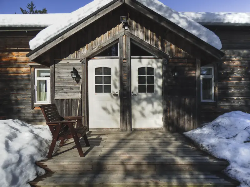 Sonniger Eingang zur Blockhütte der Saija Lodge während einer geführten Rundreise in Finnisch Lappland bei Sonnenschein.