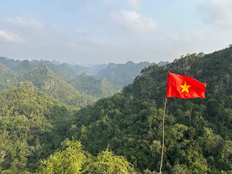 Die rote vietnamesische Flagge weht im Wind über einer weiten, dschungelbewachsenen Karstlandschaft in Nordvietnam.