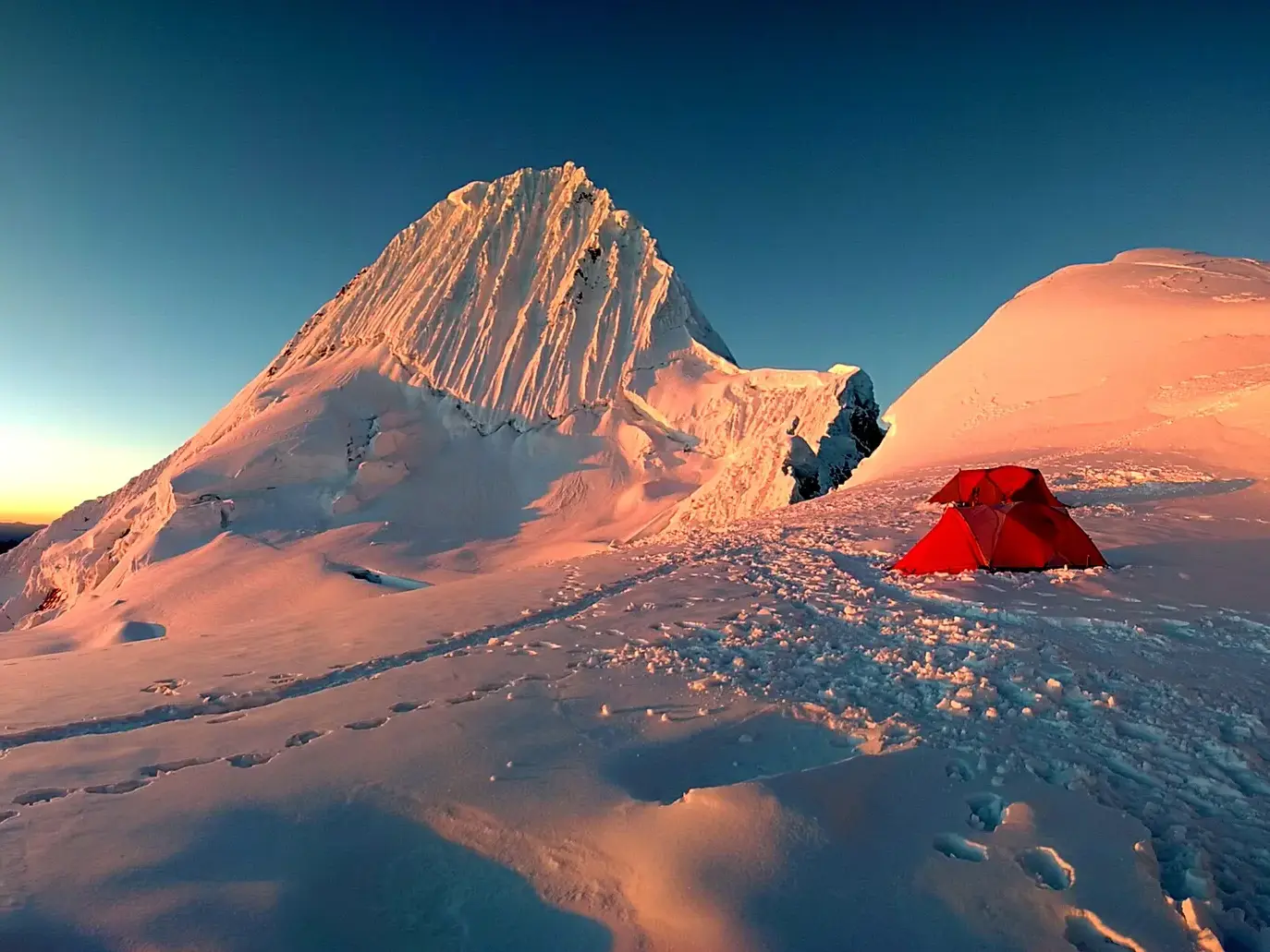 Rotes Zelt im Hochlager der Alpamayo-Expedition in der Cordillera Blanca, während der schneebedeckte Gipfel im Morgenrot leuchtet.