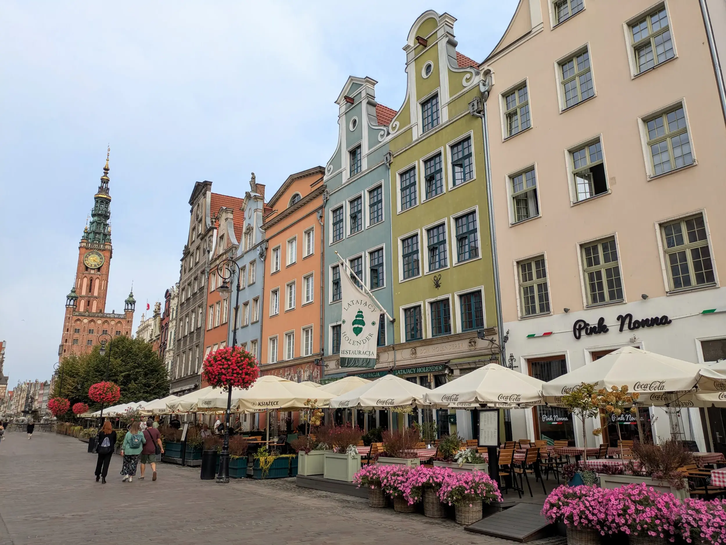 Blick auf bunte Giebelhäuser und Straßencafés in der Danziger Rechtstadt mit dem historischen Rathausturm im Hintergrund.