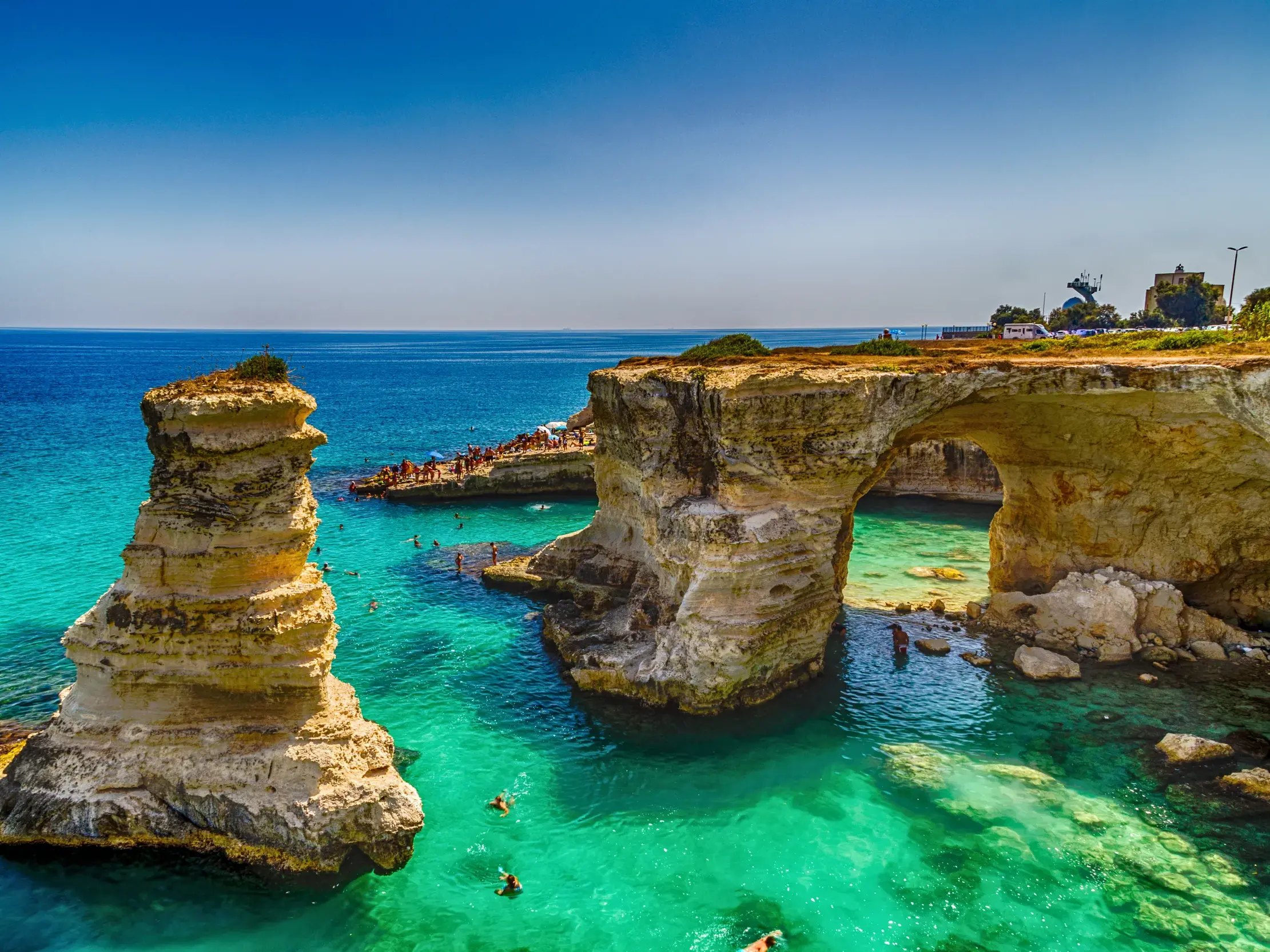 Luftaufnahme der bizarren Felsformationen bei Torre del Orso in Apulien, wo Menschen im leuchtend türkisen Meer schwimmen.