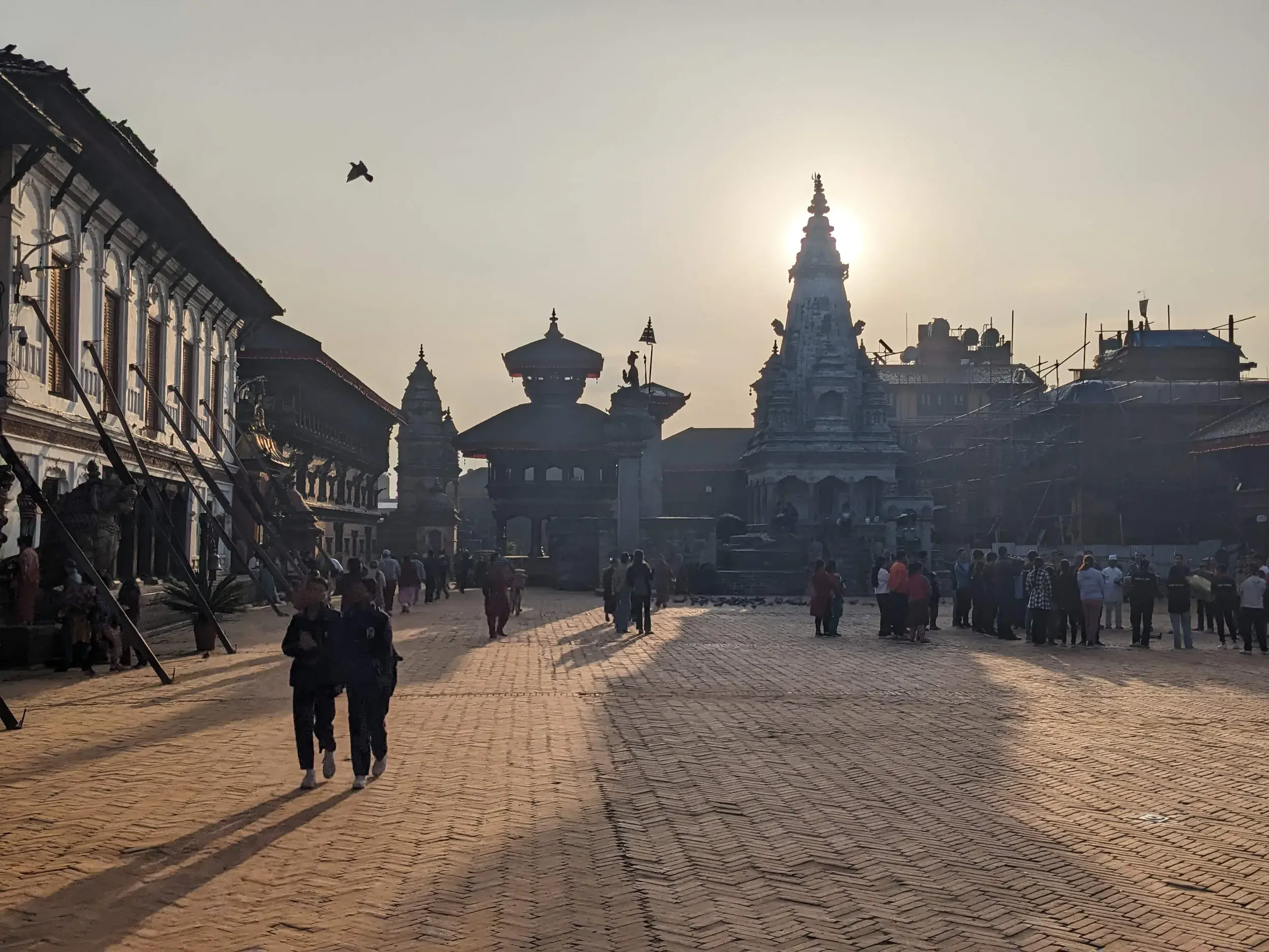Belebter Durbar Square in Kathmandu mit historischen Pagoden und Tempeln, die sich im Gegenlicht der Abendsonne abzeichnen.