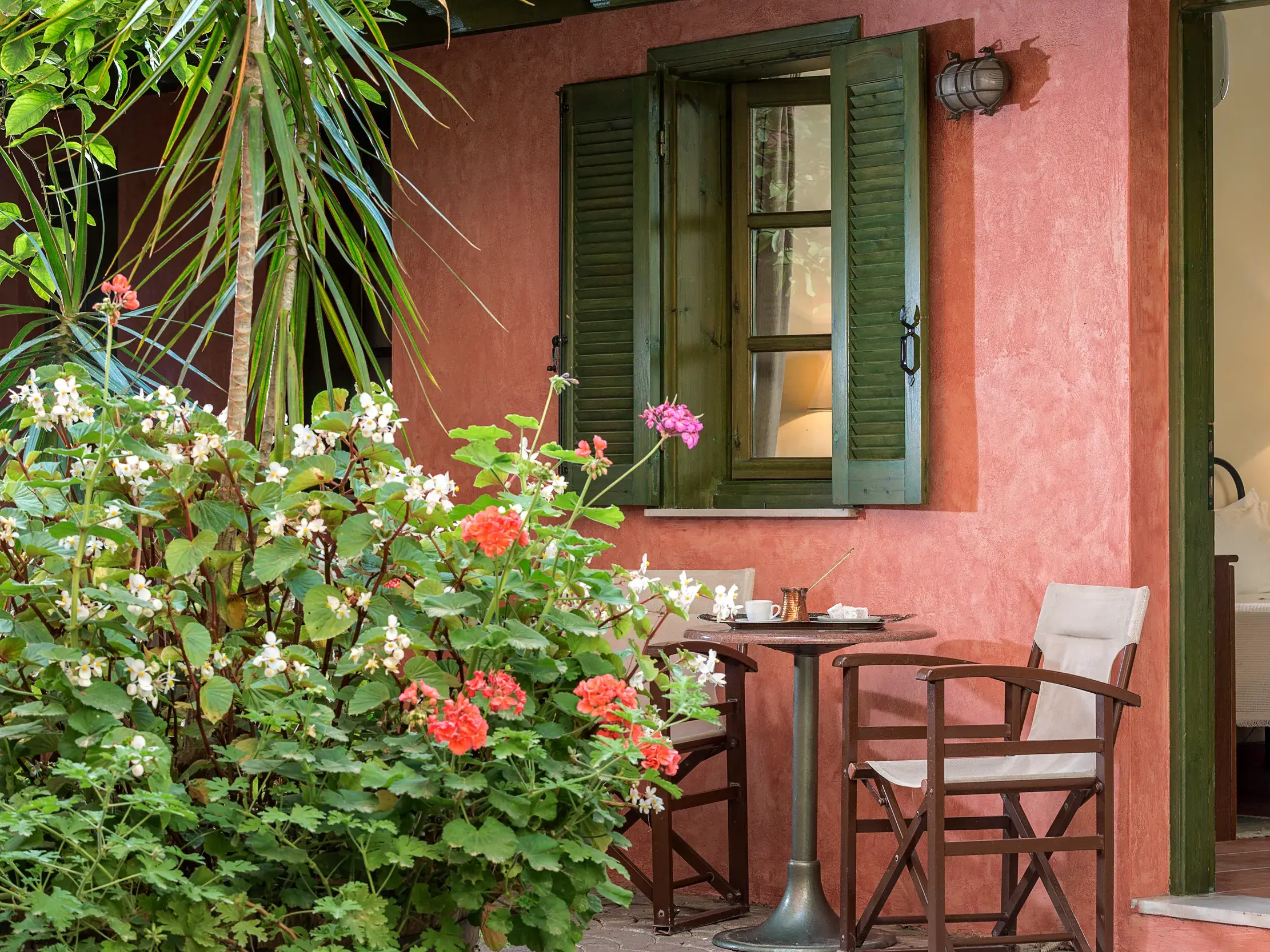 Private, blumengeschmückte Terrasse des Hotel Nafsimedon in Nauplia mit einer Sitzgelegenheit und Blick ins Zimmer.
