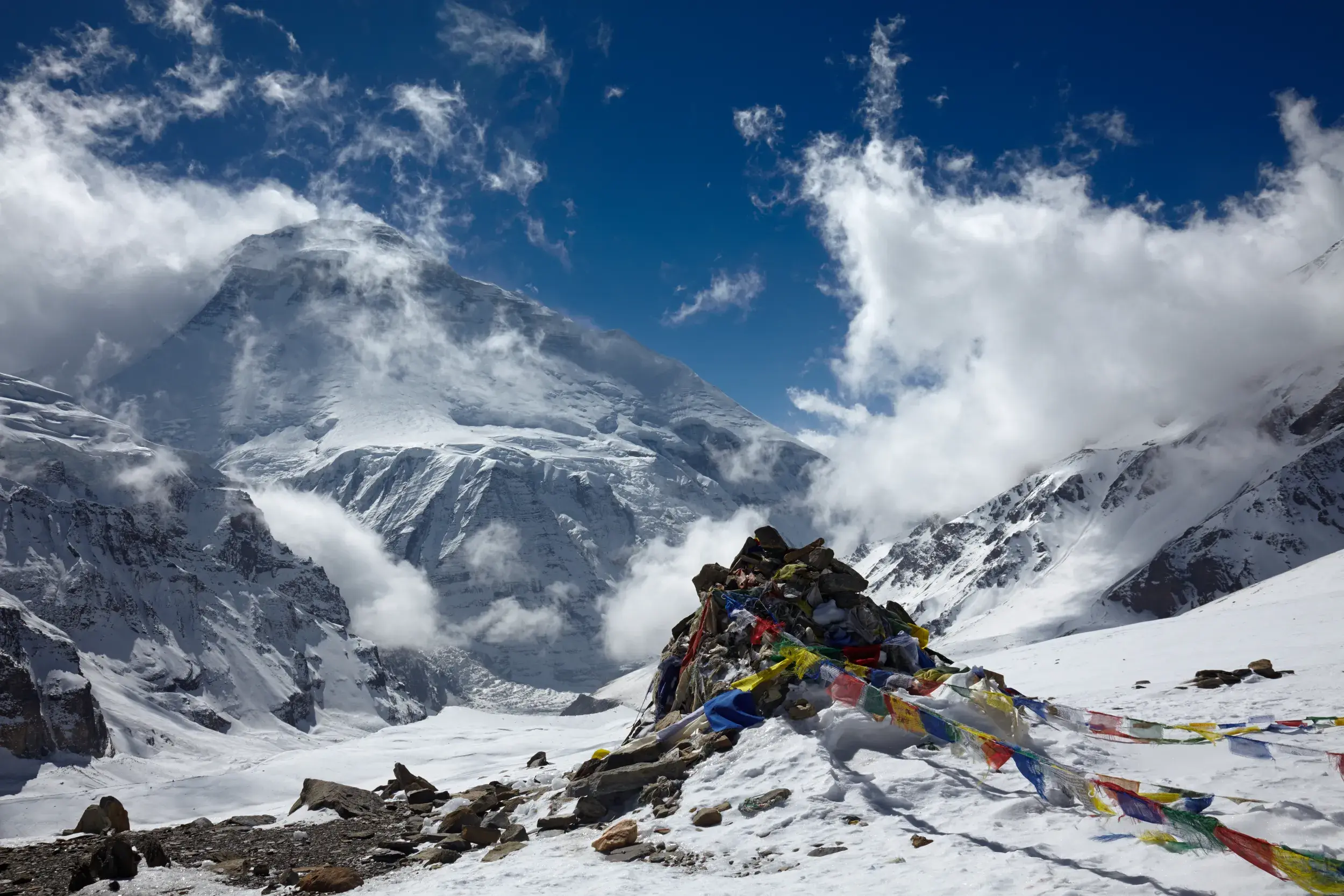 Farbenfrohe Gebetsfahnen auf einem Steinhaufen am French Col vor dem schneebedeckten Gipfel des Dhaulagiri in Nepal.