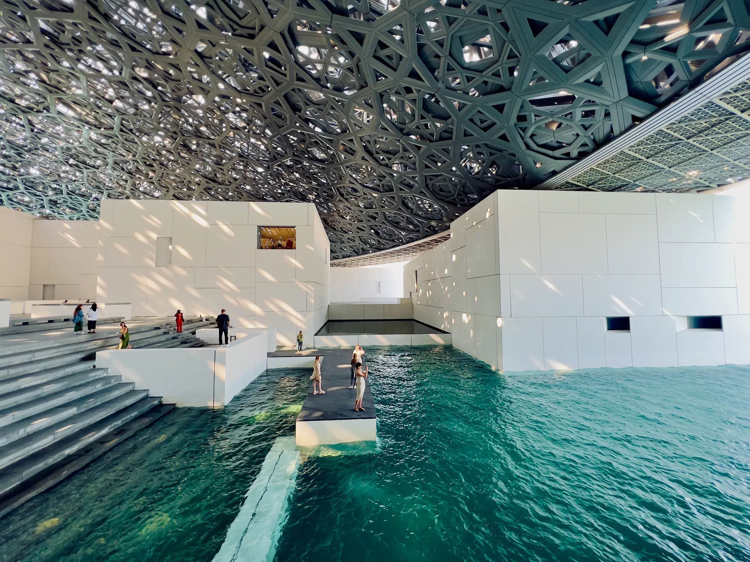 Studienreise-Teilnehmer im Louvre Abu Dhabi, wo Licht durch die Kuppel auf die von Wasser umgebenen Ausstellungsgebäude fällt.