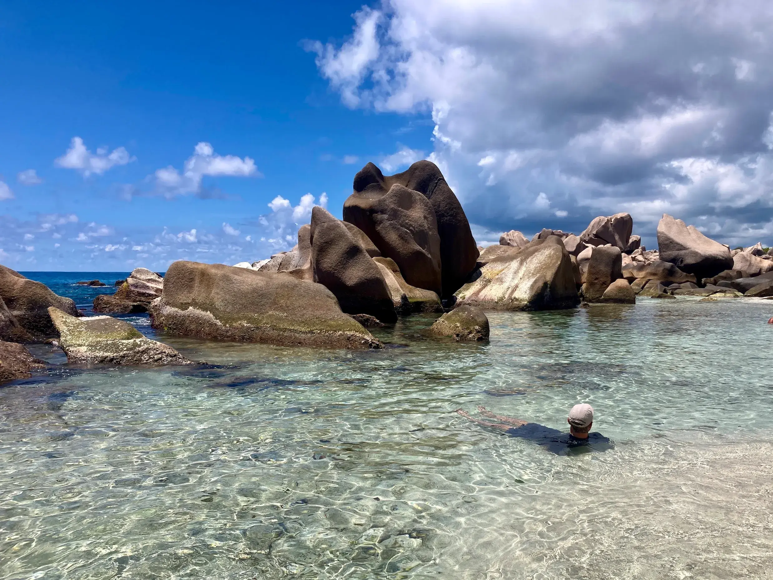 Ein Reiseteilnehmer badet im kristallklaren Wasser vor der Kulisse der einzigartigen Granitfelsen an einem Strand der Seychellen.