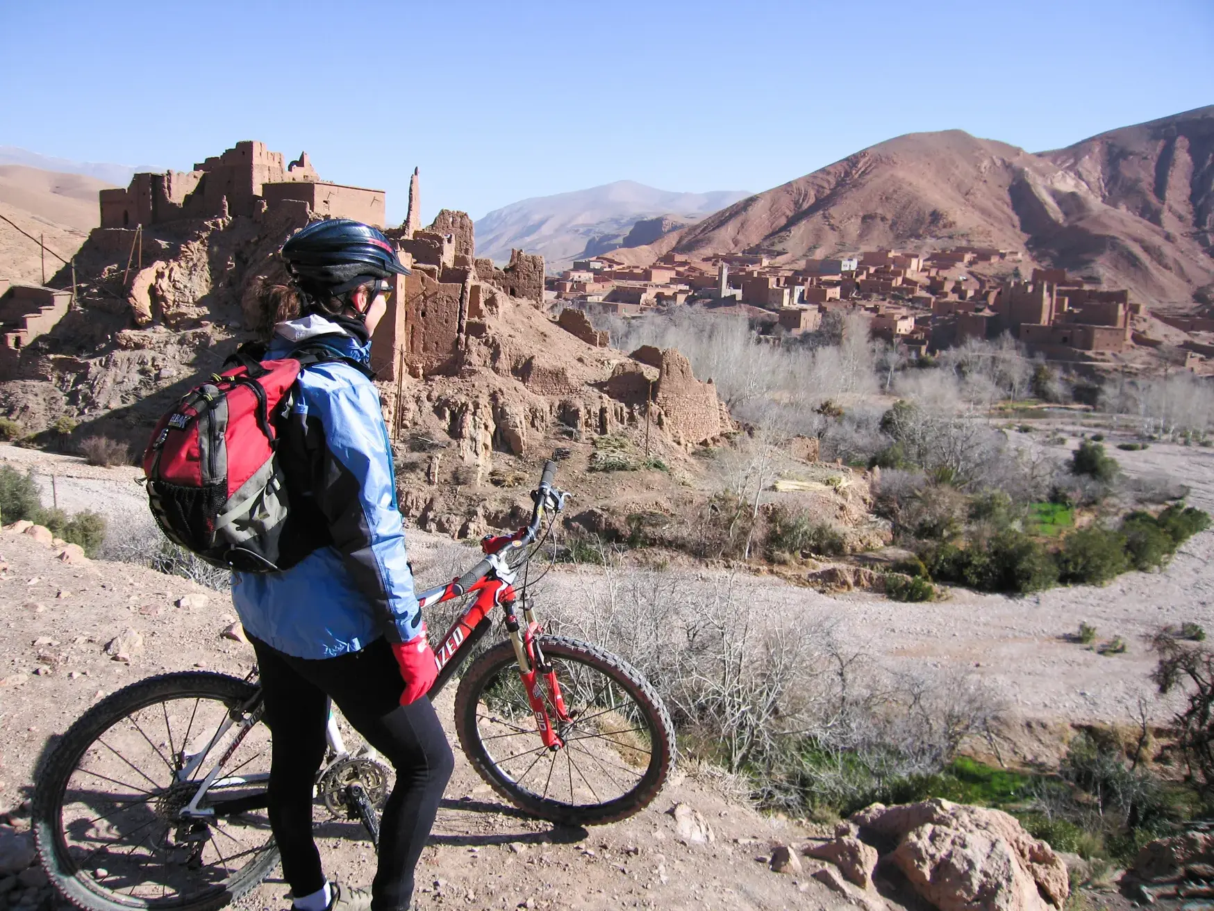 Mountainbiker bei einer Pause mit Blick auf die traditionellen Lehmburgen in einem Tal der Dades-Schlucht in Marokko.