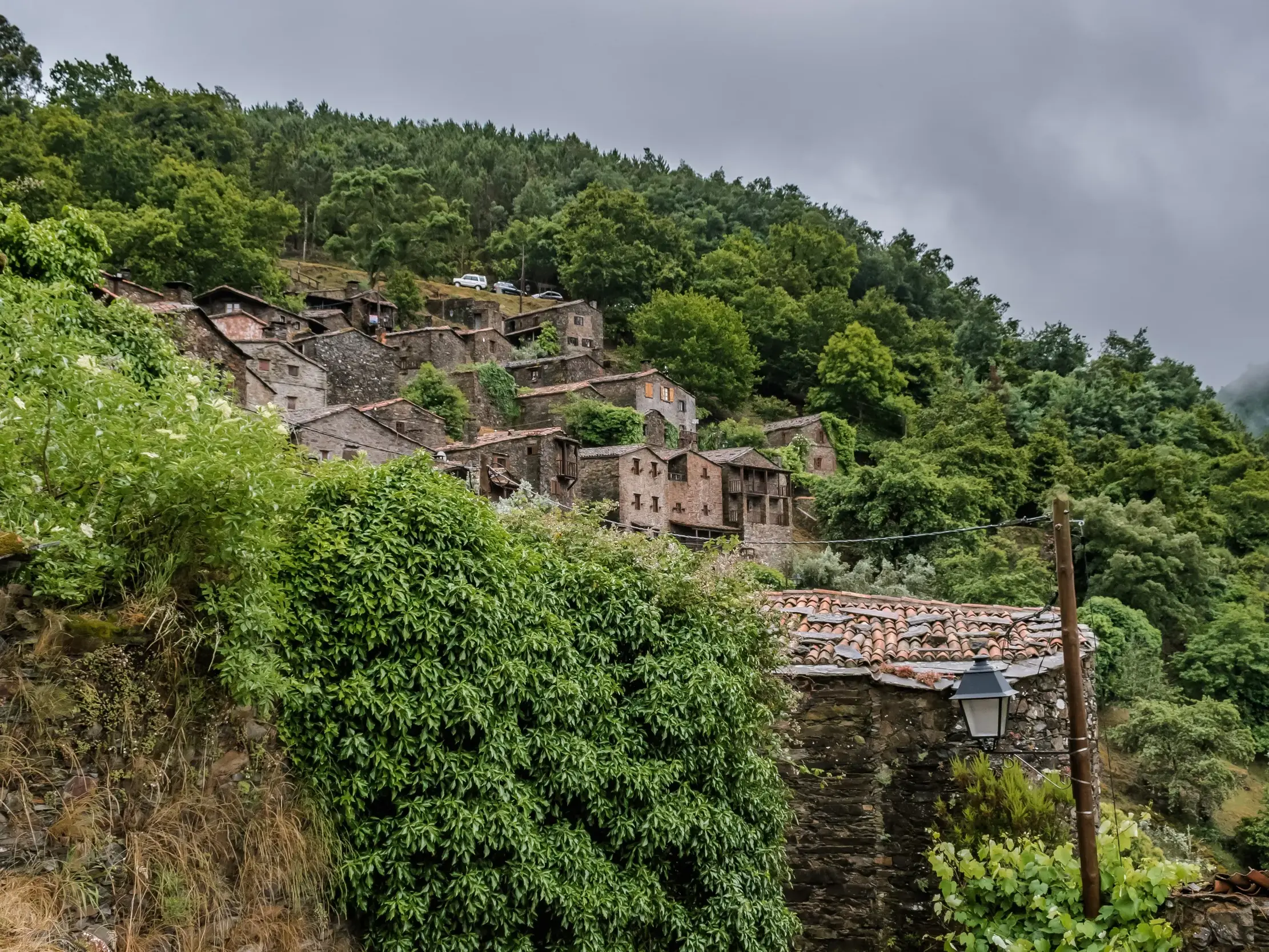 Ein traditionelles Schieferdorf mit Steinhäusern schmiegt sich an einen bewaldeten Berghang in der Serra da Lousã in Portugal.