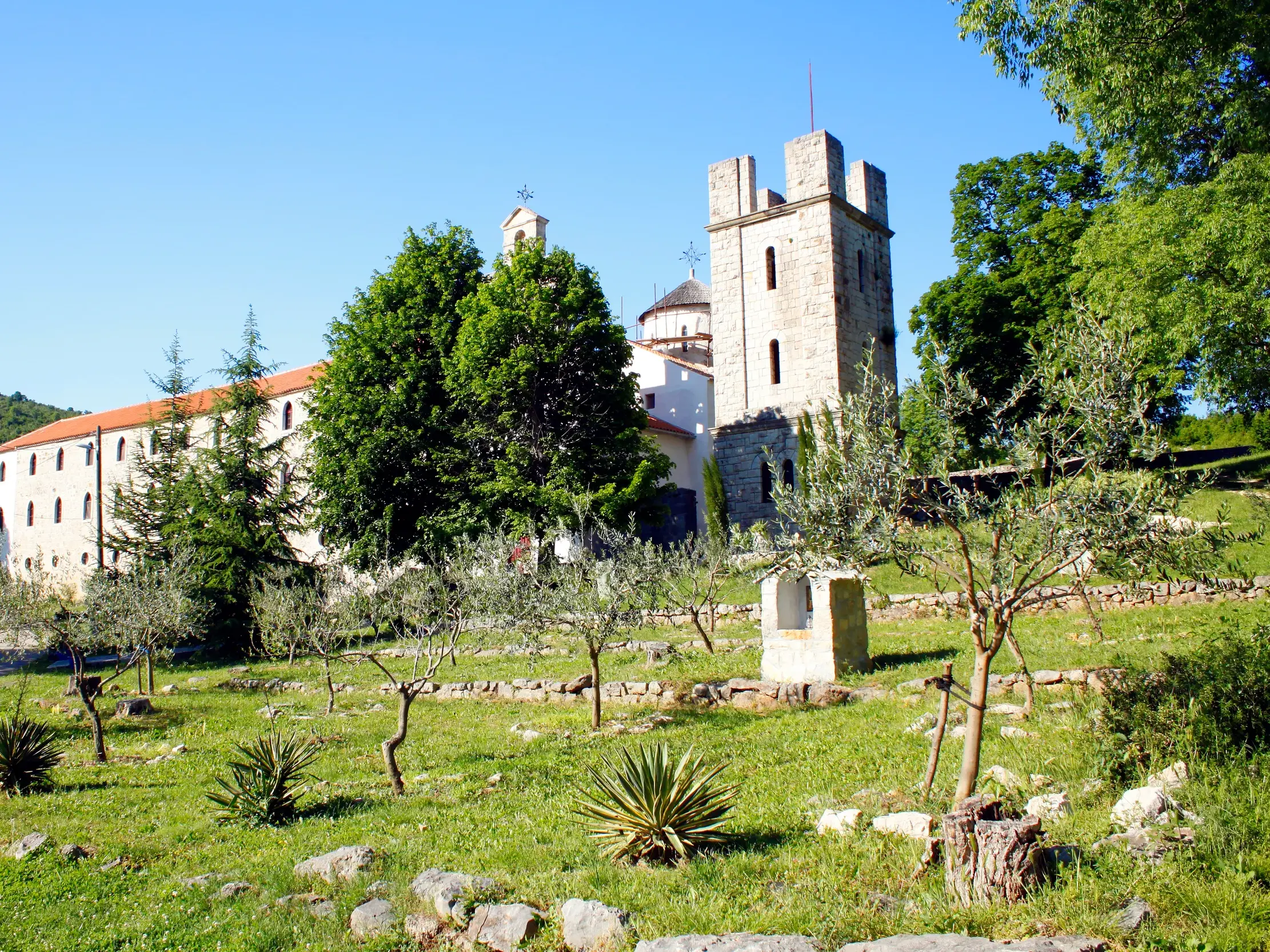 Das historische Kloster Krupa in Kroatien mit seinem Steinturm, eingebettet in eine grüne Landschaft mit Olivenbäumen.