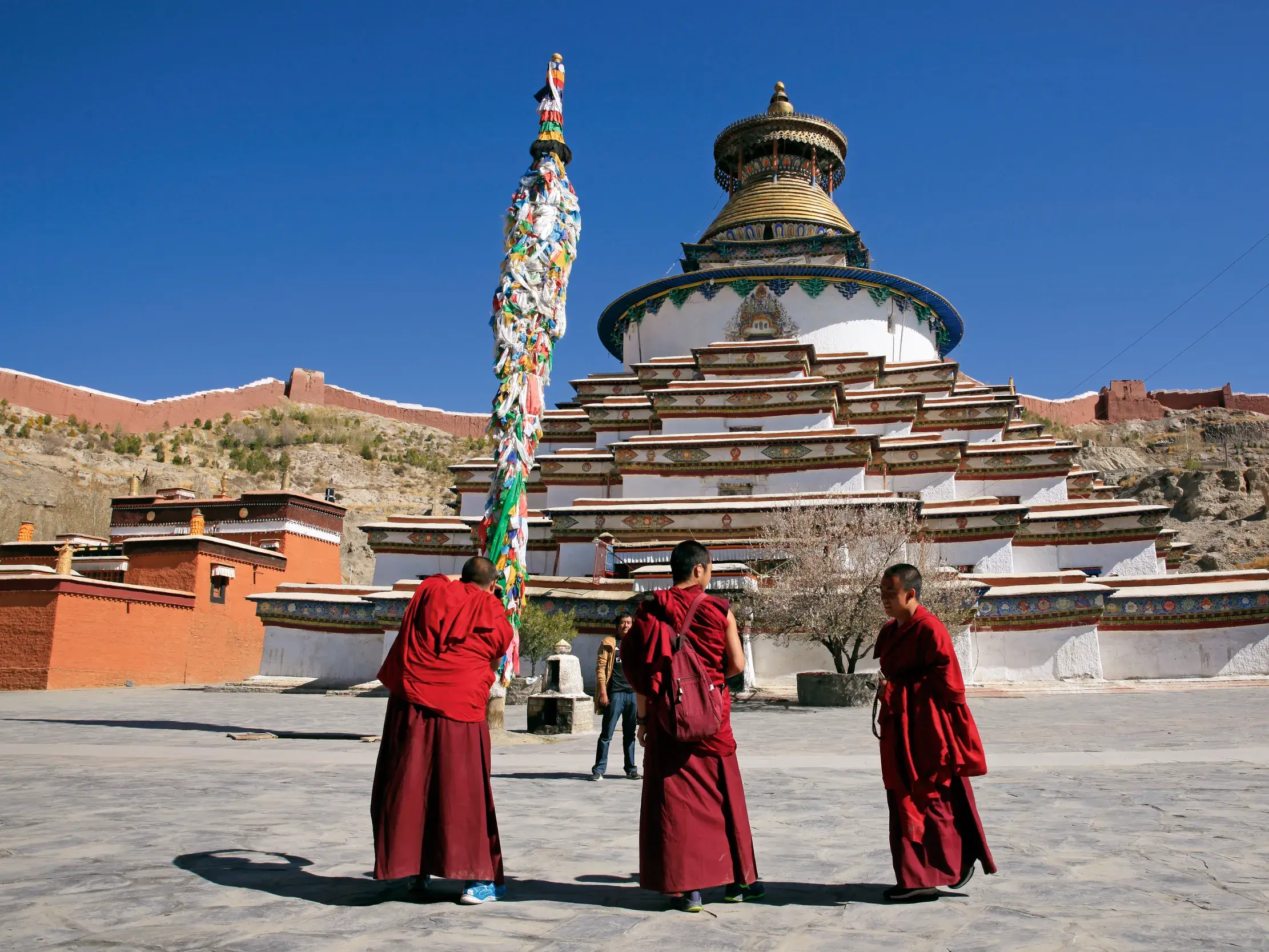Drei tibetische Mönche in roten Roben vor dem mehrstöckigen Kumbum Stupa der Klosteranlage Palkhor Chöde in Gyantse.