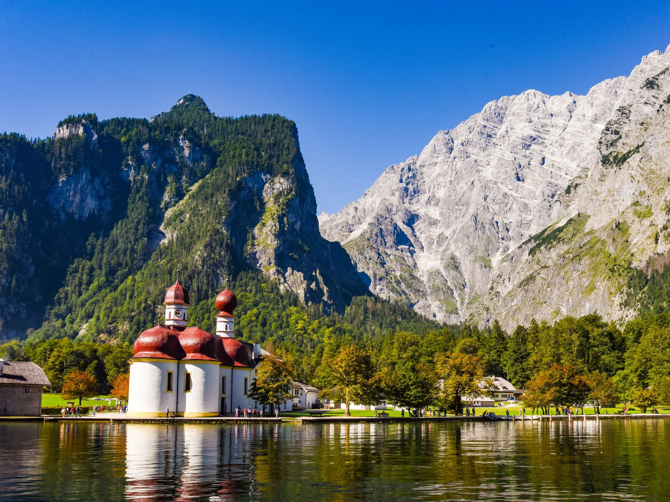 Die berühmte Kapelle St. Bartholomä spiegelt sich im klaren Wasser des Königssees vor der Felskulisse des Nationalpark Berchtesgaden.