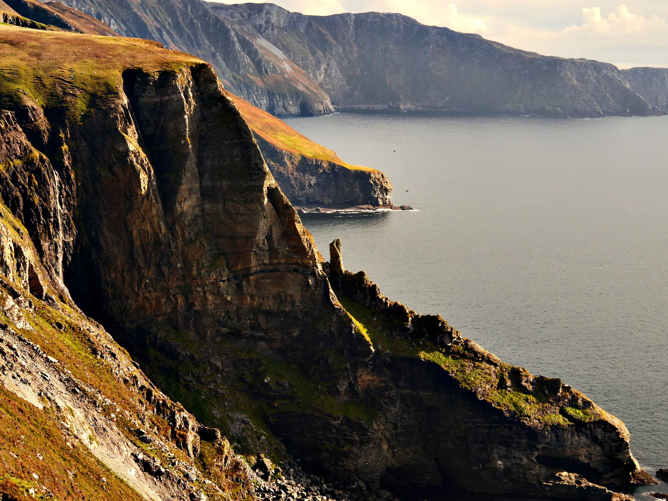 Hohe, grasbewachsene Steilklippen der Slieve League ragen bei einer Wanderreise in Irland aus dem ruhigen Atlantik.