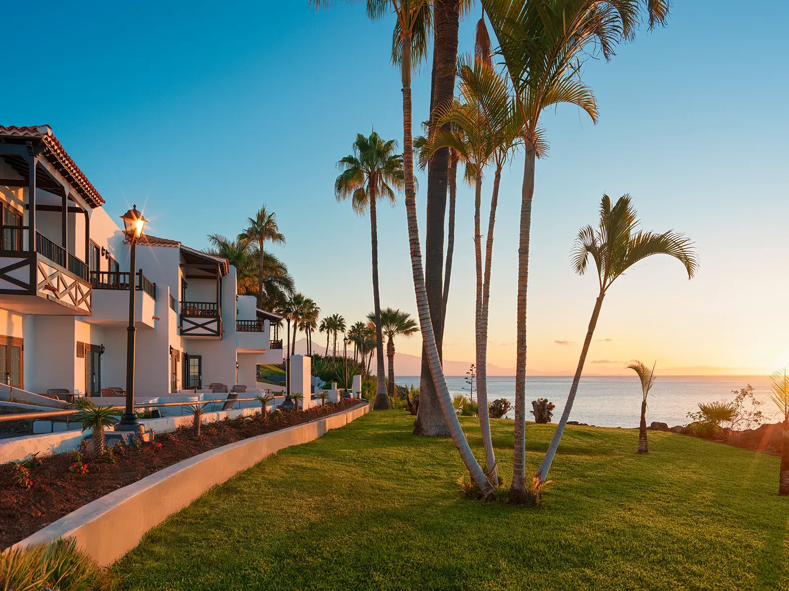 Die idyllische Gartenanlage des Hotels Jardín Tecina auf La Gomera mit Palmen und Blick auf den Atlantik bei Sonnenuntergang.
