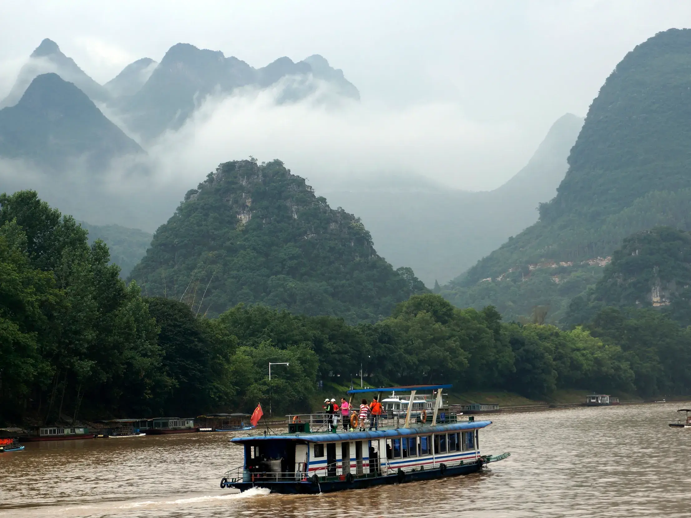 Reisegruppe auf einem Ausflugsboot auf dem Li-Fluss, umgeben von der berühmten, nebligen Karstlandschaft bei Yangshuo in China.