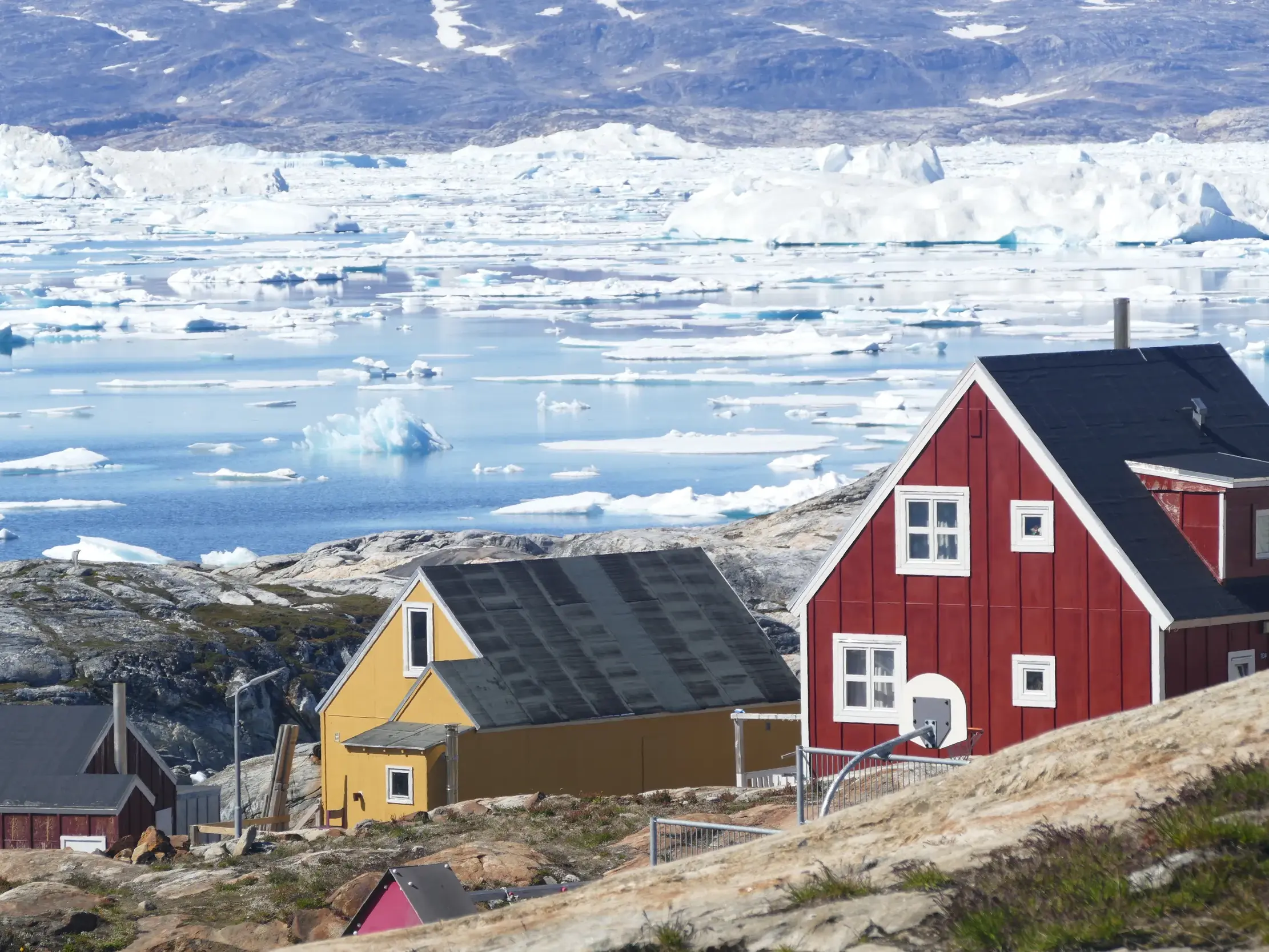 Bunte Holzhäuser der Inuit-Siedlung Tiniteqilaaq an der felsigen Küste des eisfylten Sermilik-Fjords in Ostgrönland.