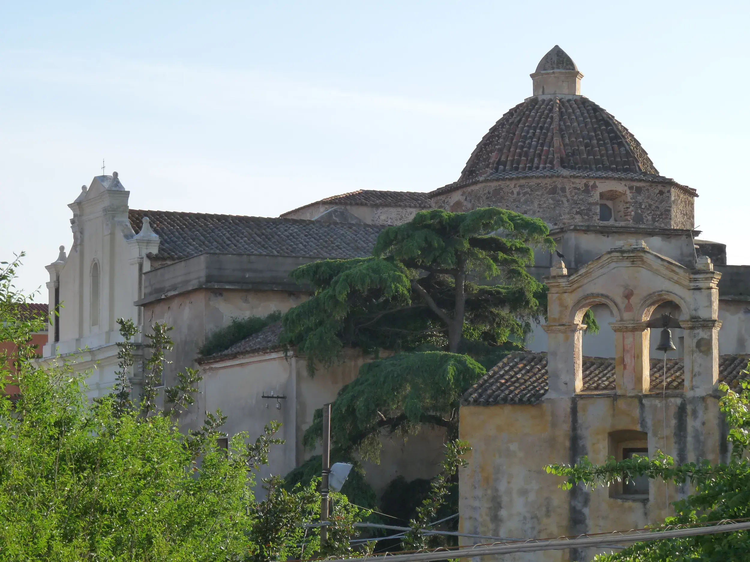 Historische Steinkuppel der Kirche Santa Maria degli Angeli in Santu Lussurgiu, umgeben von grünen Bäumen auf Sardinien.