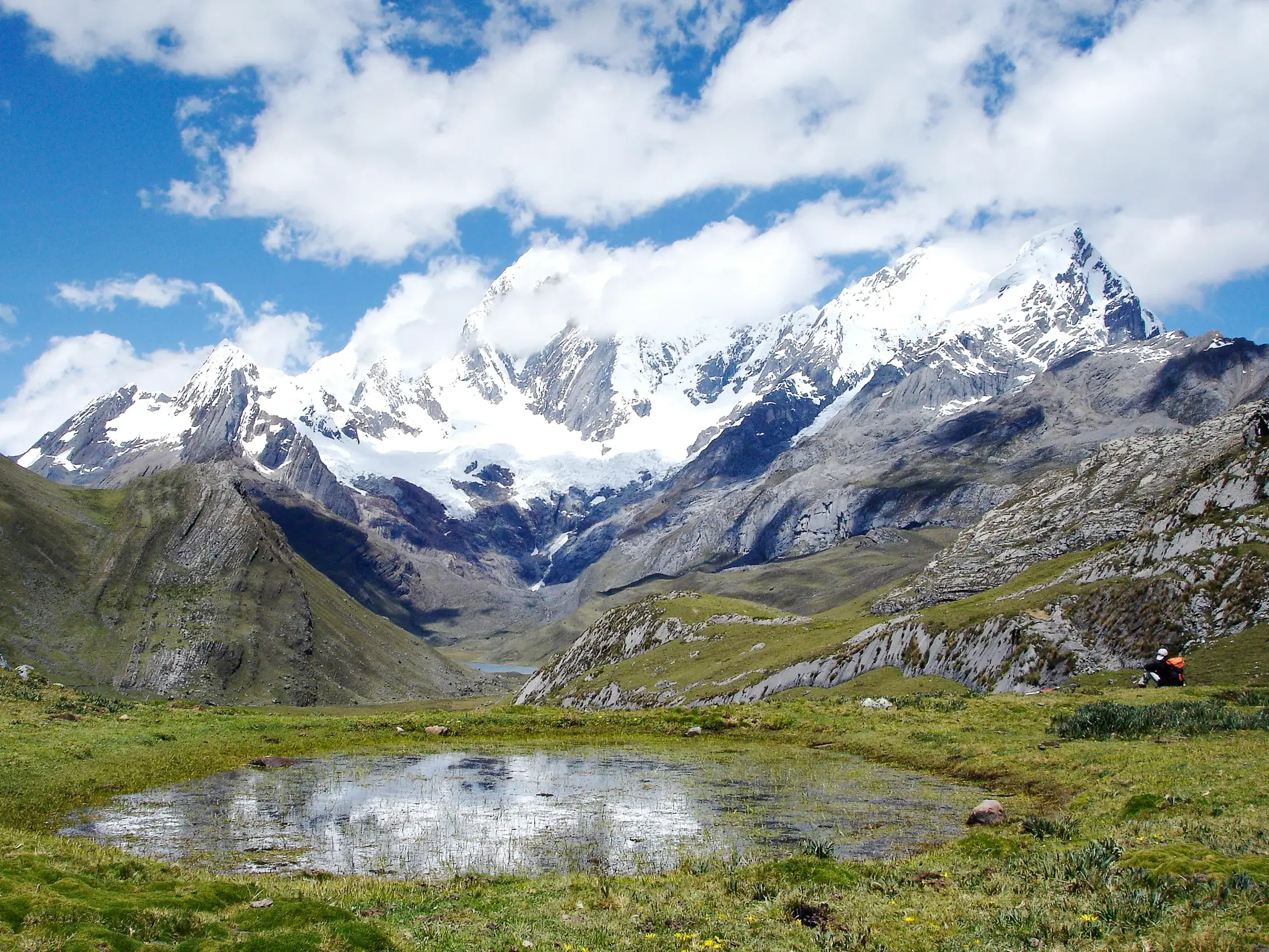 Wanderer macht eine Pause an einem klaren Bergsee mit Blick auf die schneebedeckten Gipfel der Cordillera Blanca in Peru.